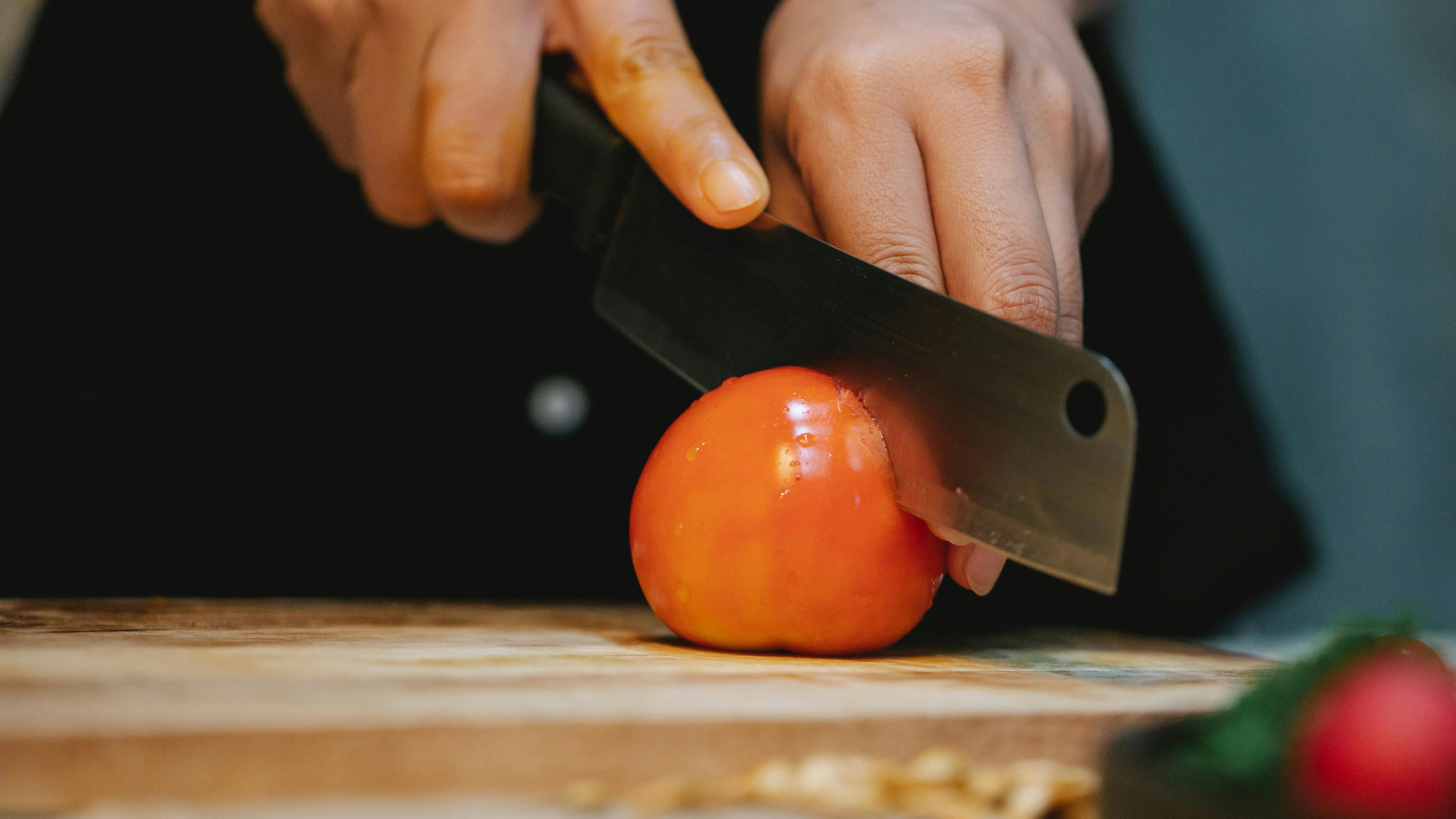 A nakiri knife slicing a tomato.