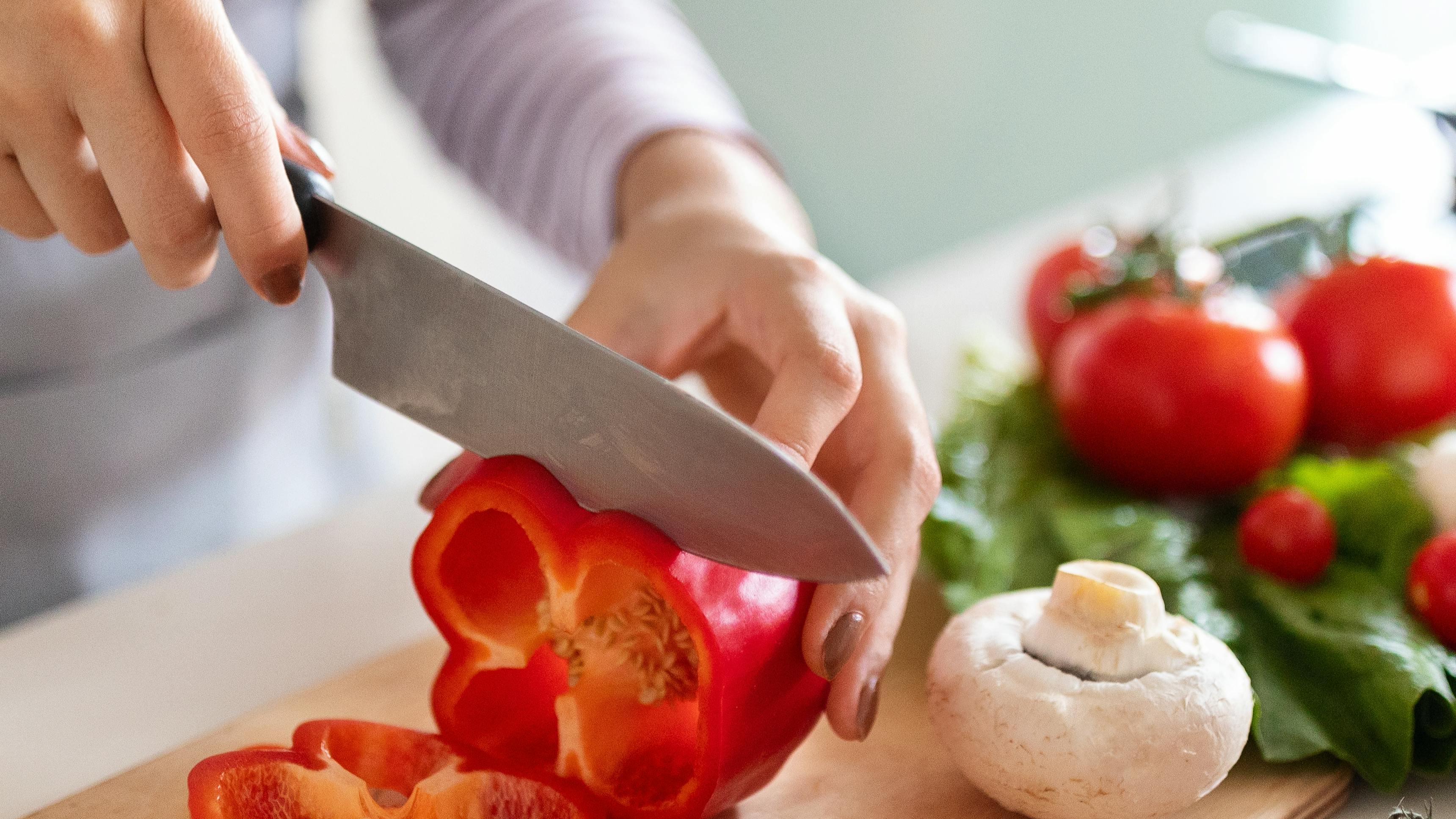 Close up of a woman's hands as she cuts peppers with a kitchen knife.