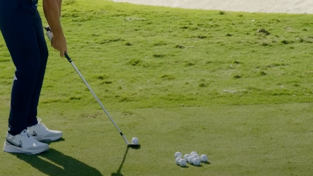A golfer hitting balls with a golf club as several golf balls sit in front of him. 