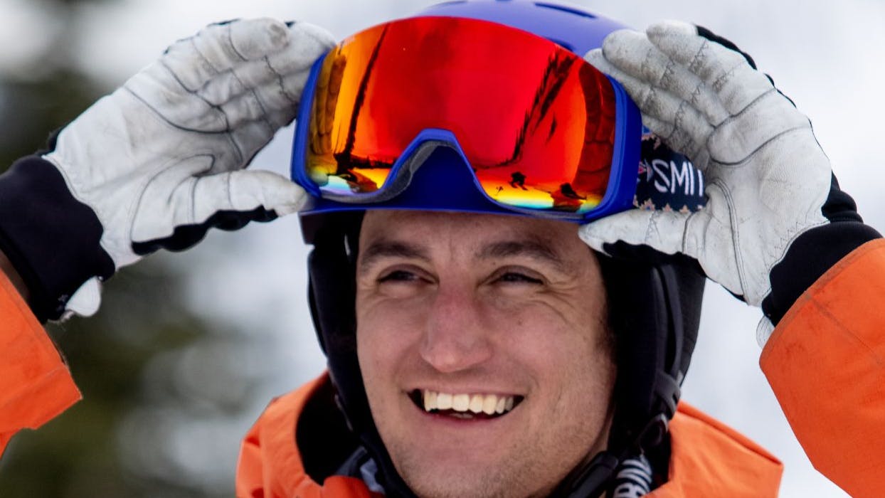 A man putting his goggles on his helmet as he smiles. 