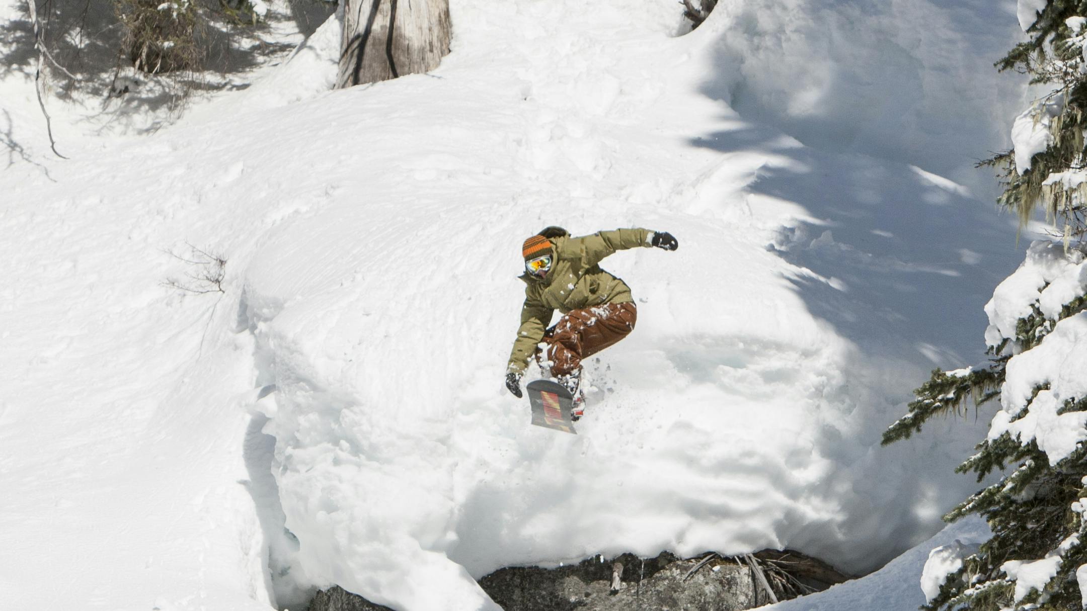 A snowboarder snowboards off a jump in a densely wooded area.