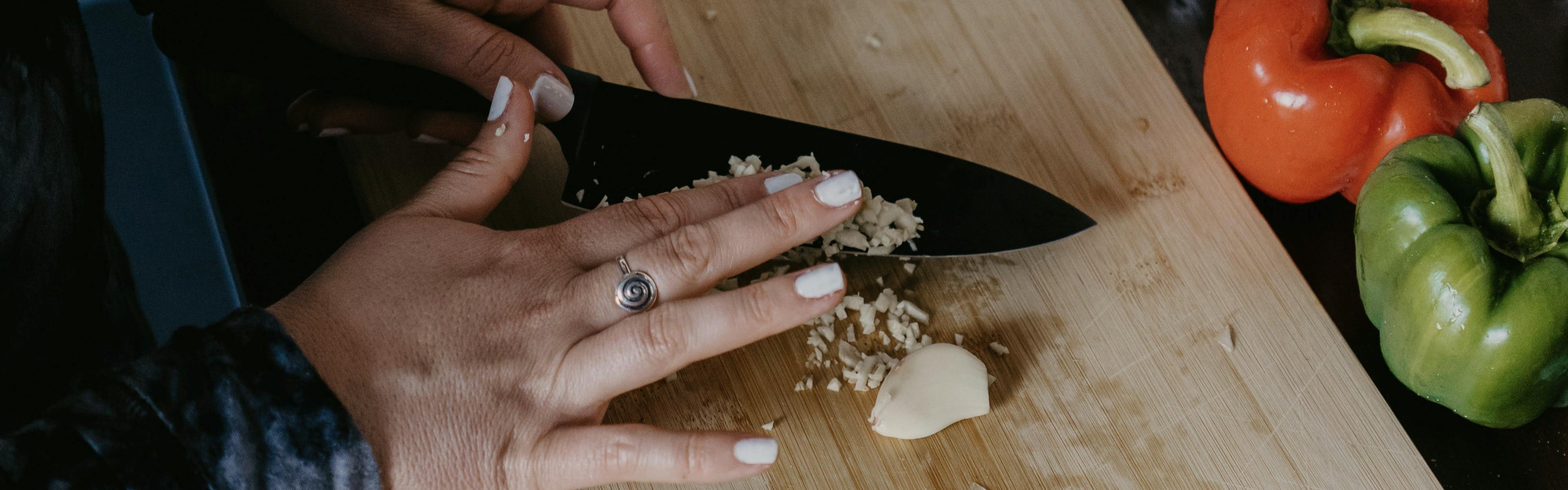 Close up of a woman using a knife to chop garlic. 