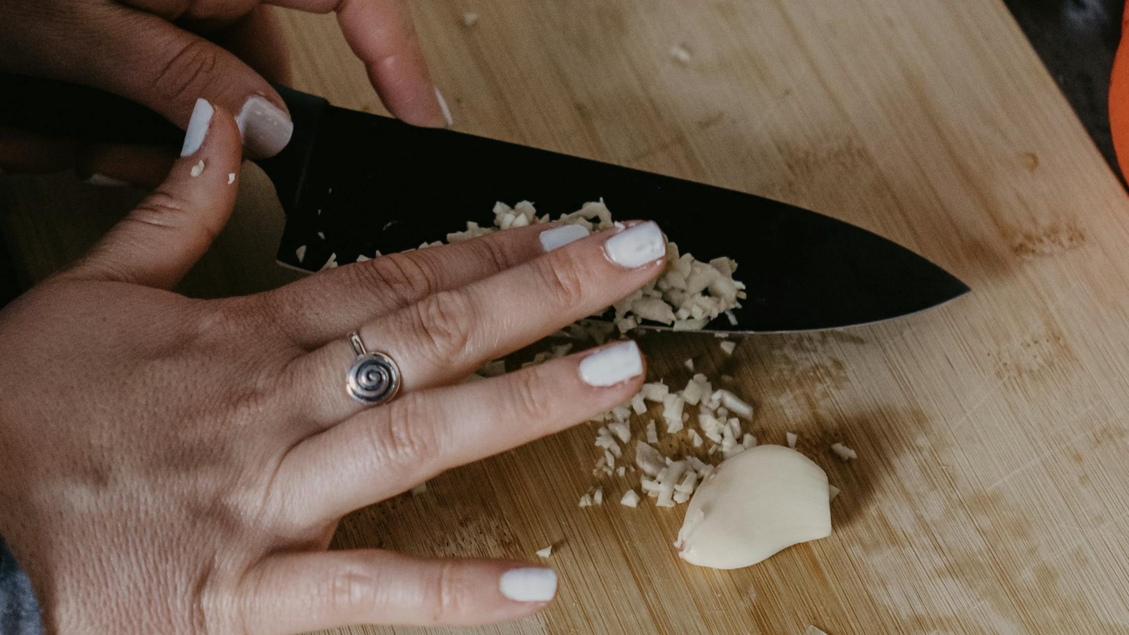 Close up of a woman using a knife to chop garlic. 