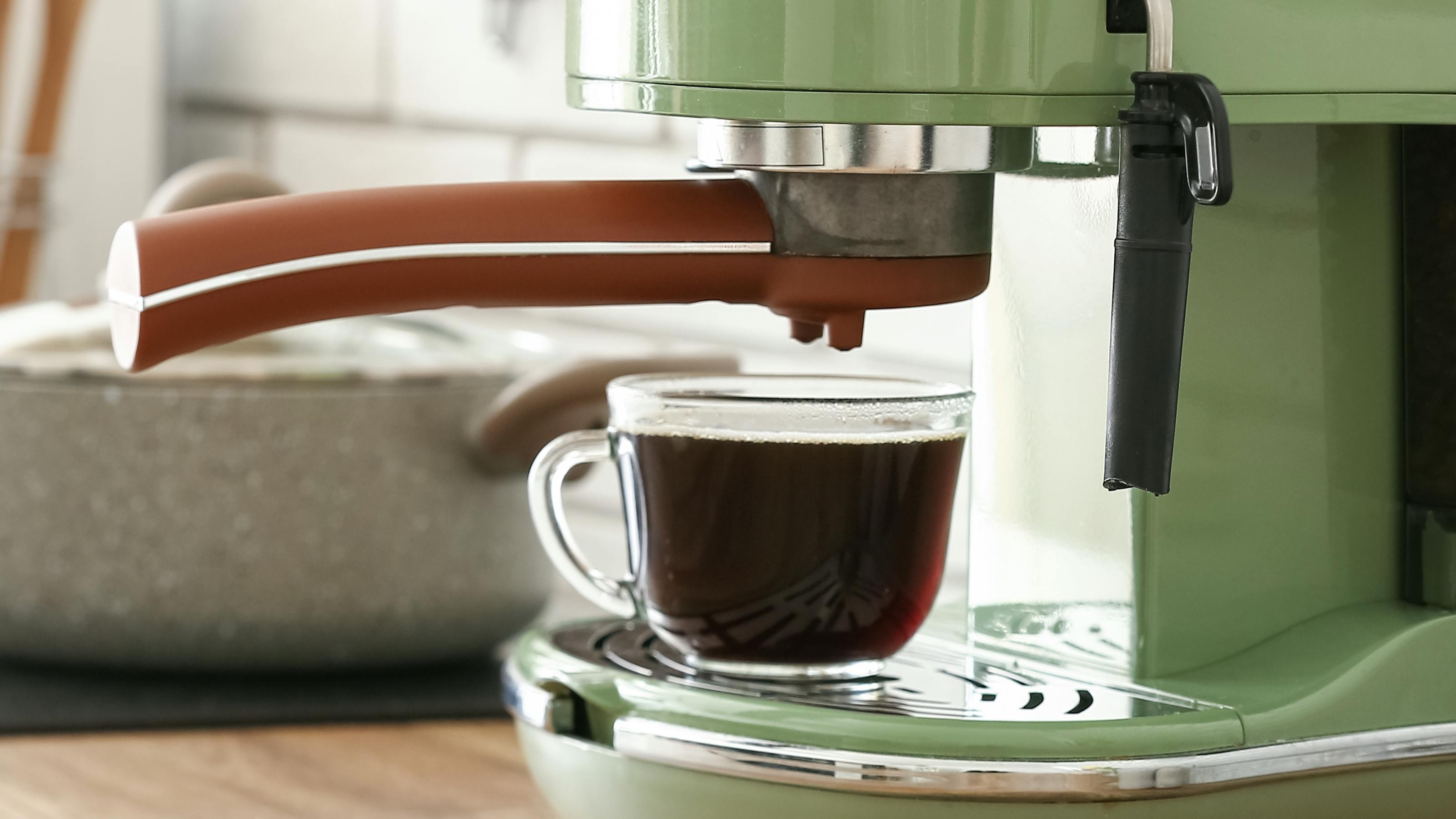 A cup of espresso under an espresso machine on a kitchen counter. 