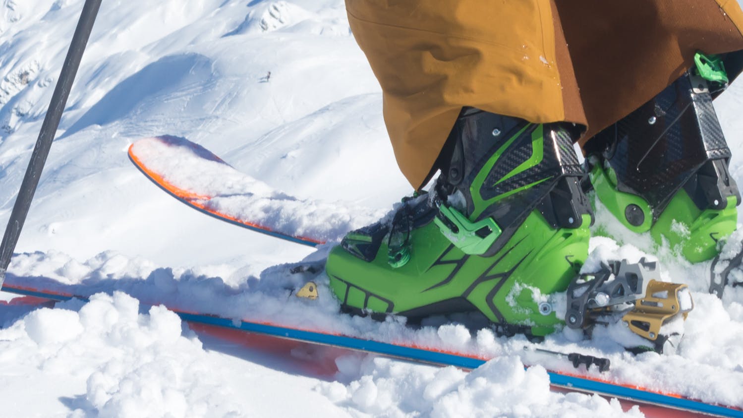 Close up of a skiers ski boots as hes standing at the top of a snowy pass.