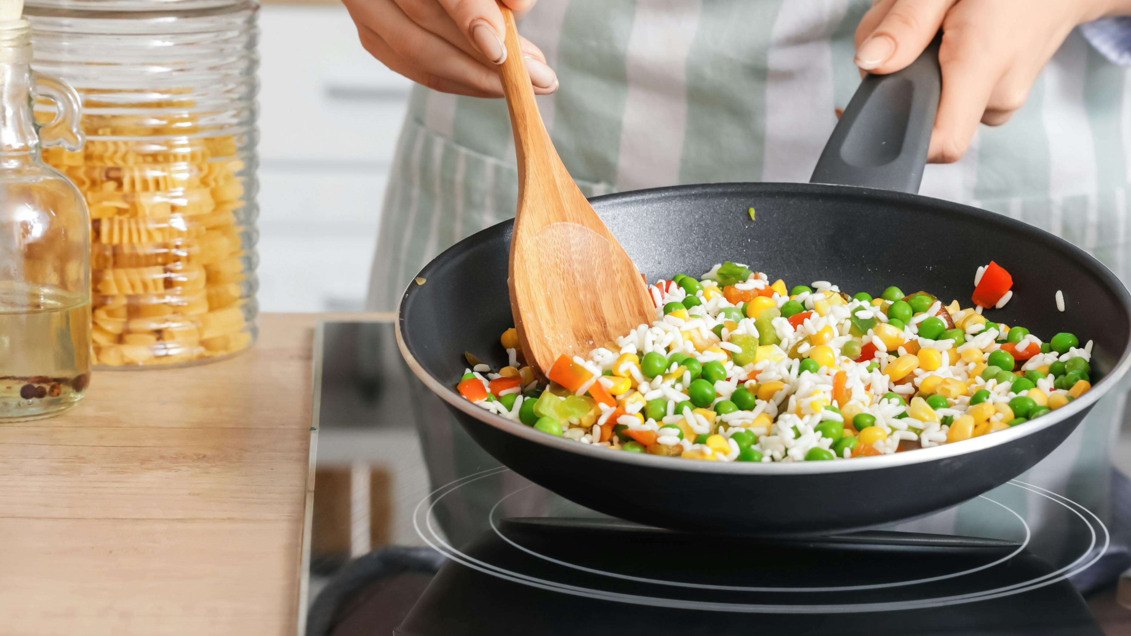 Close up of someone cooking rice and veggies in a cast iron pan. 