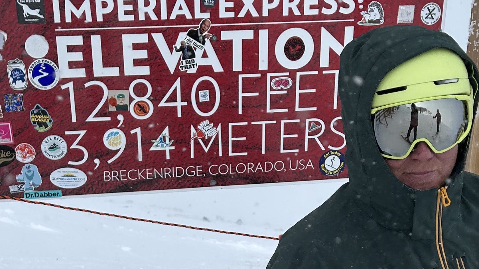 A skier standing in the Helly Hansen Men's Alpha Insulated Jacket in front of a sign that tells the elevation. 