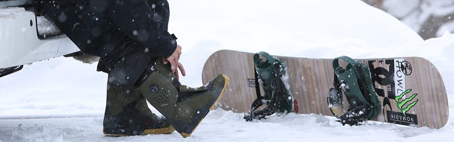 A snowboarder lacing up some DC Snowboard Boots as a snowboard sits on the ground. 