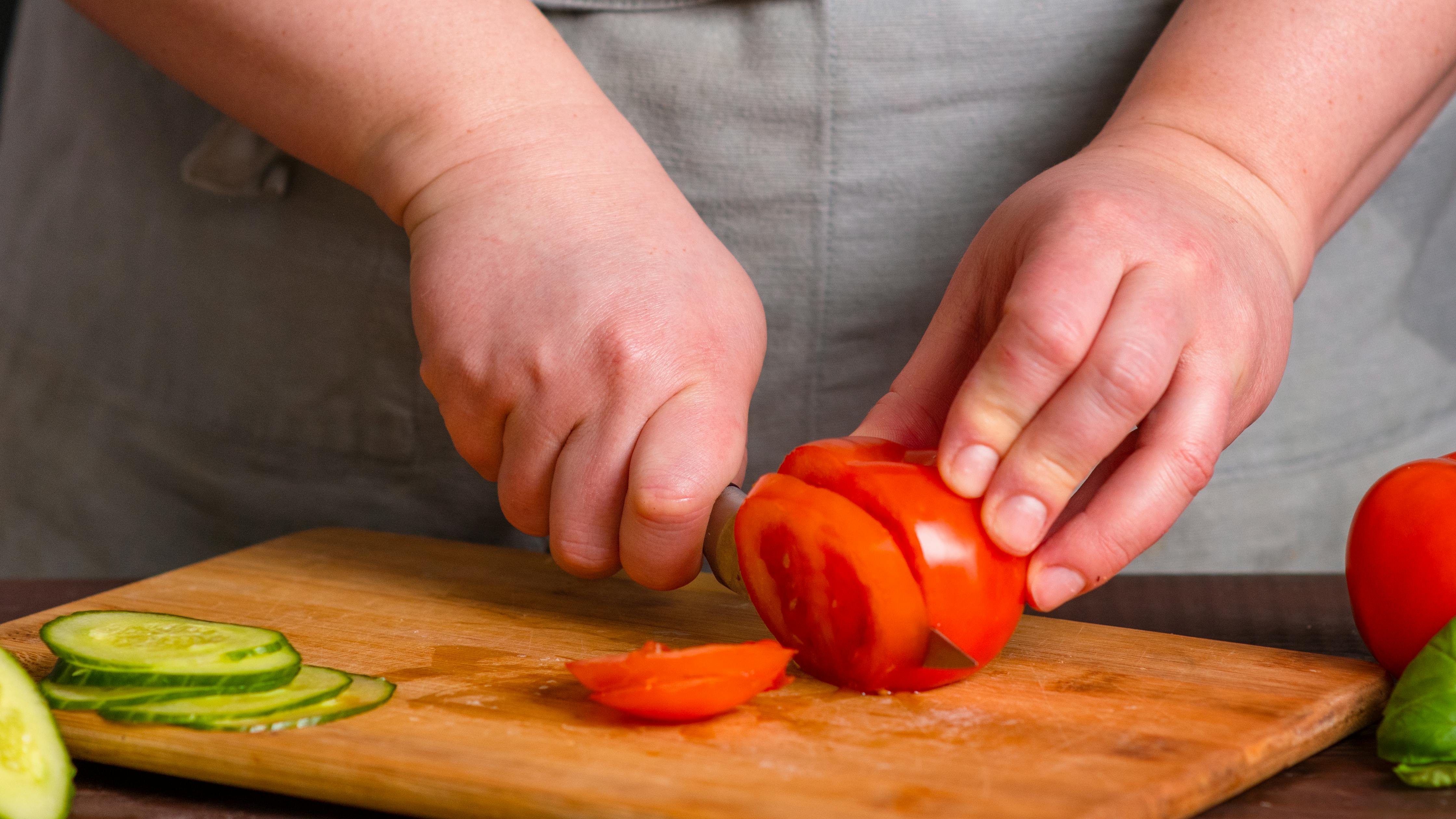 Close up of a woman cutting tomatoes on a cutting board. 
