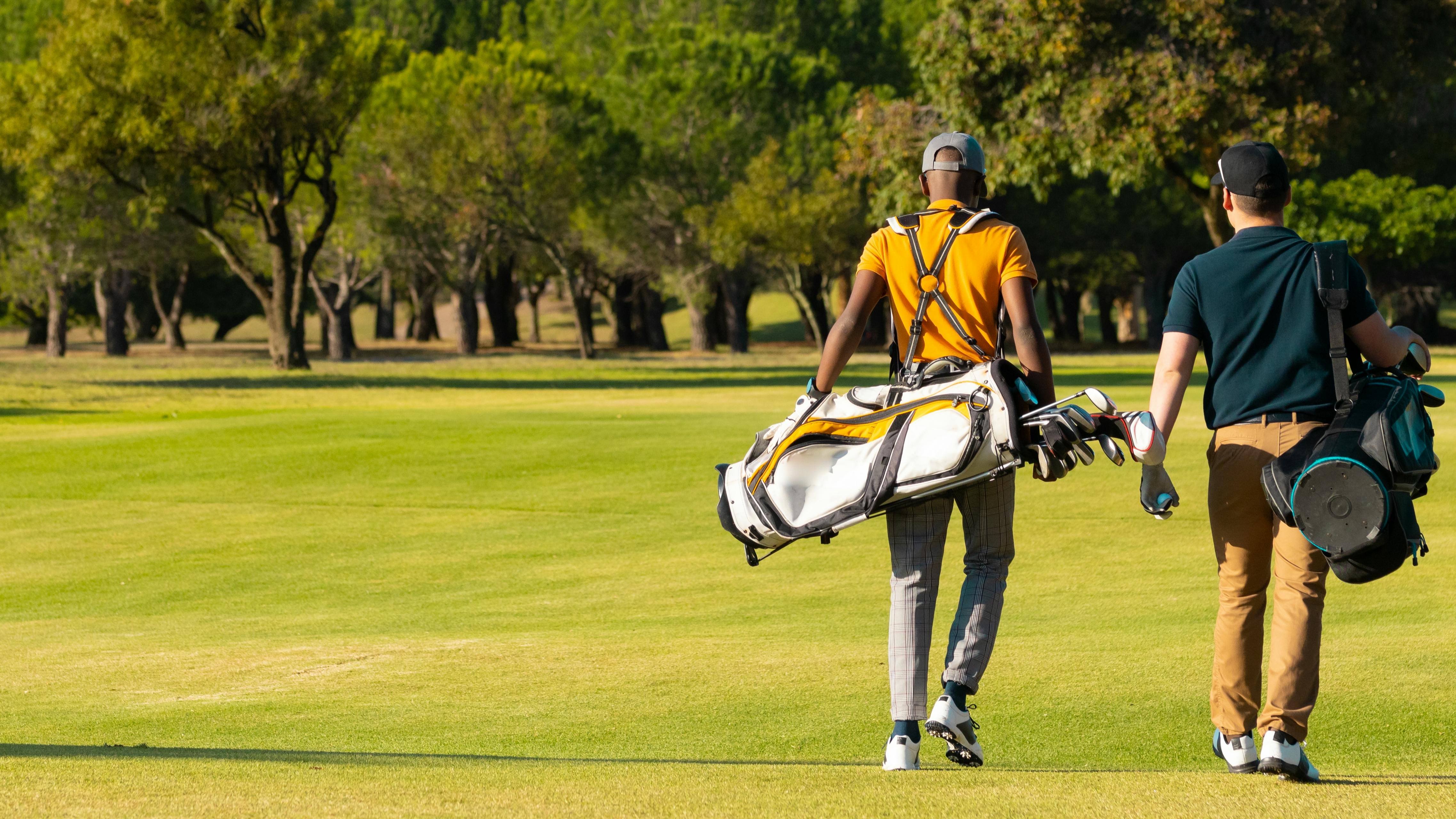 Two golfers walking along a golf course as they both carry golf bags. 