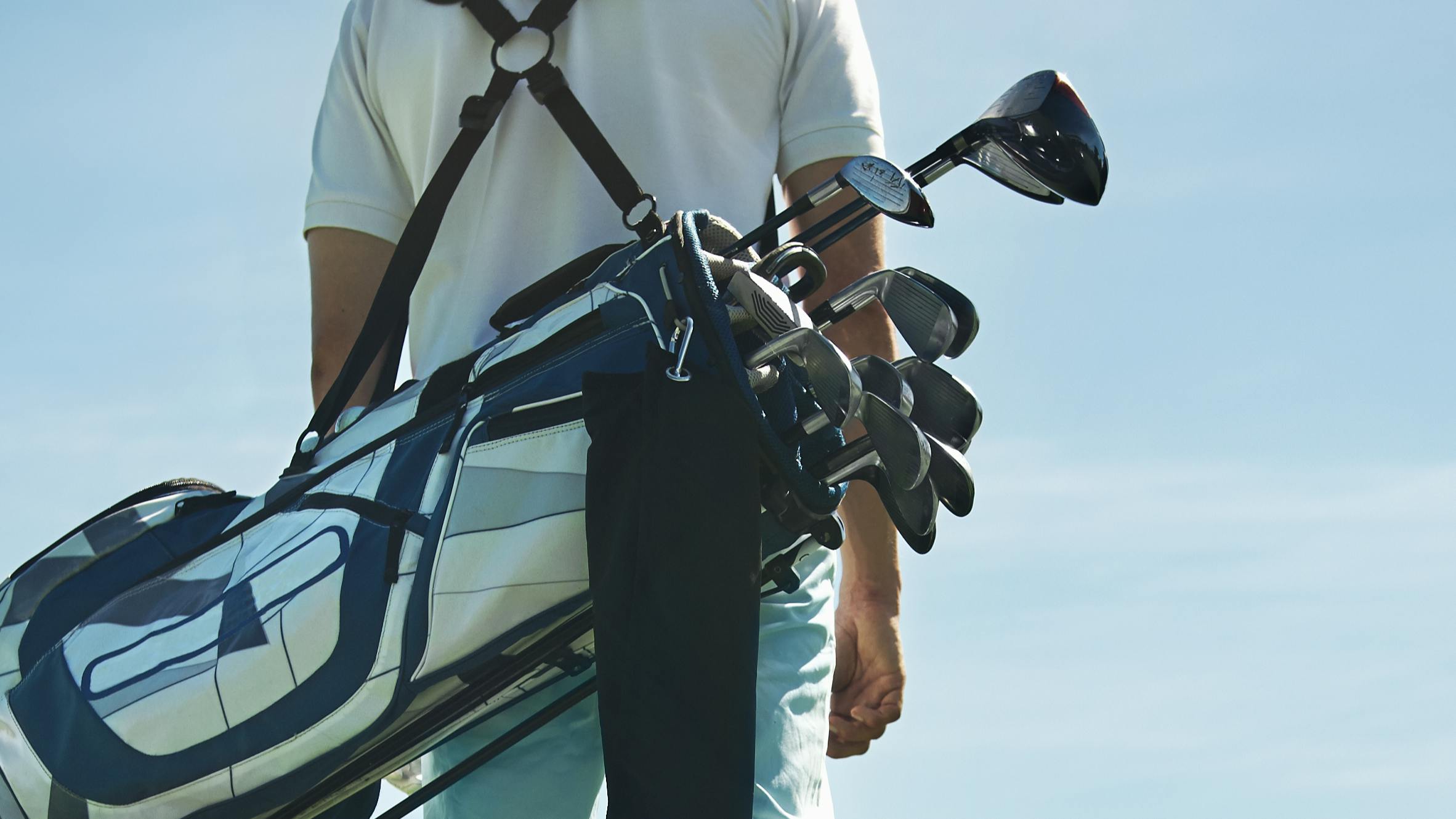 Back view of someone carrying a golf bag with clubs in it. 