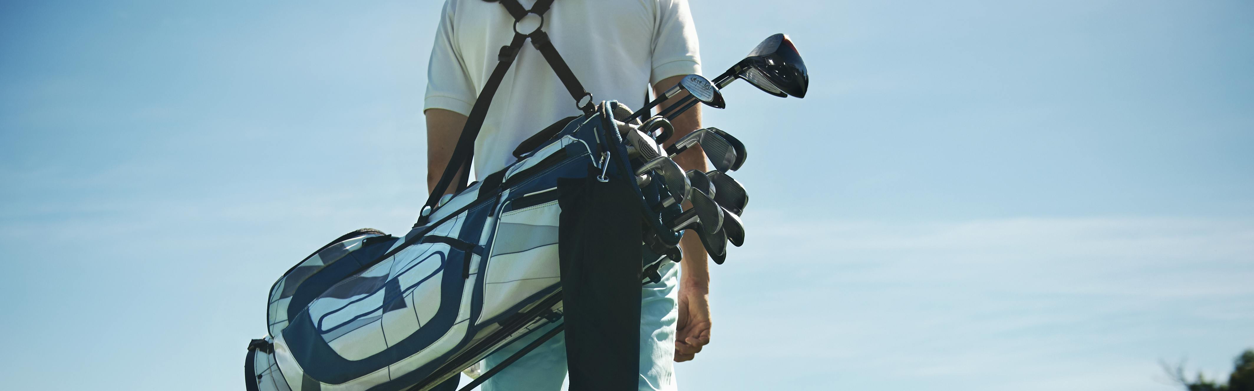 Back view of someone carrying a golf bag with clubs in it. 