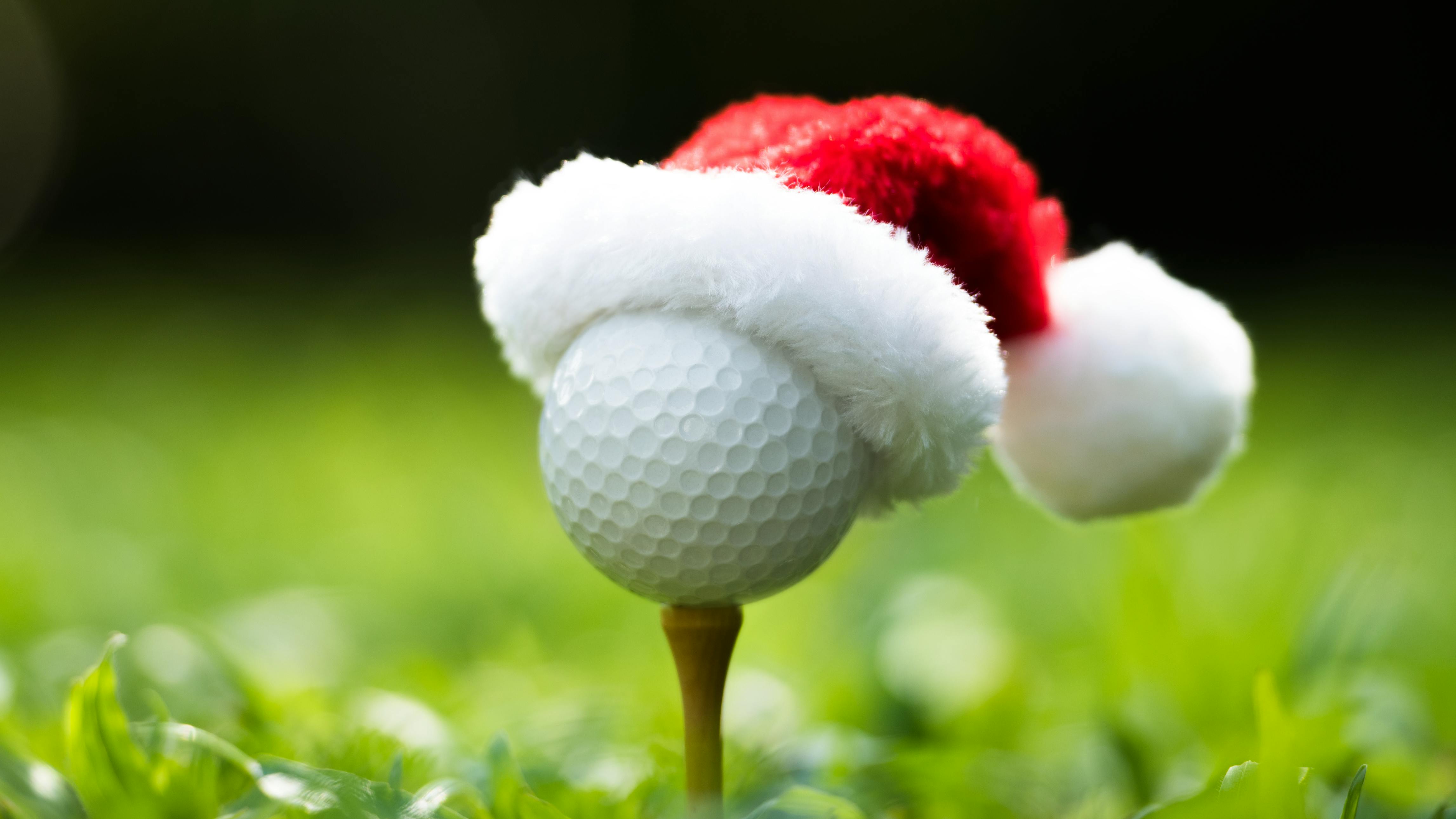 A golf ball on a tee wearing a small red and white santa hat. 