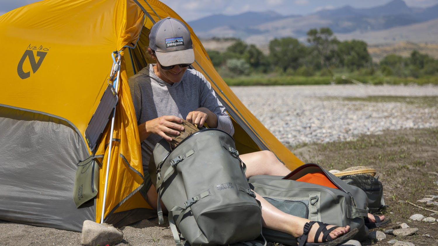 A woman putting gear into a mystery ranch pack as she sits in a tent.