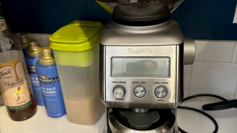 Breville Smart Grinder Pro Coffee & Espresso Grinder on kitchen counter, sugar and syrups in background.