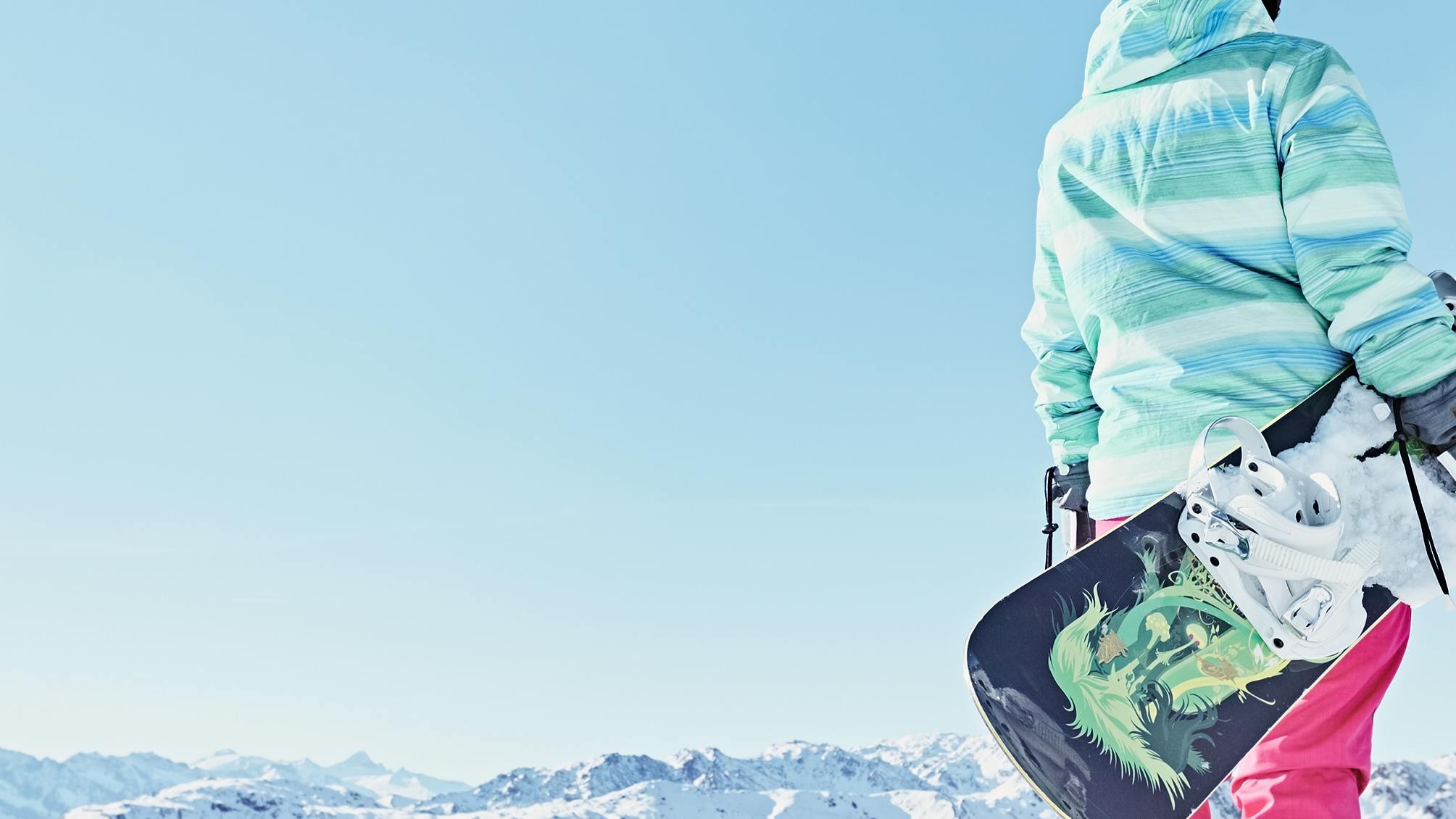 A woman standing at the top of a snowy mountain peak holding a snowboard.