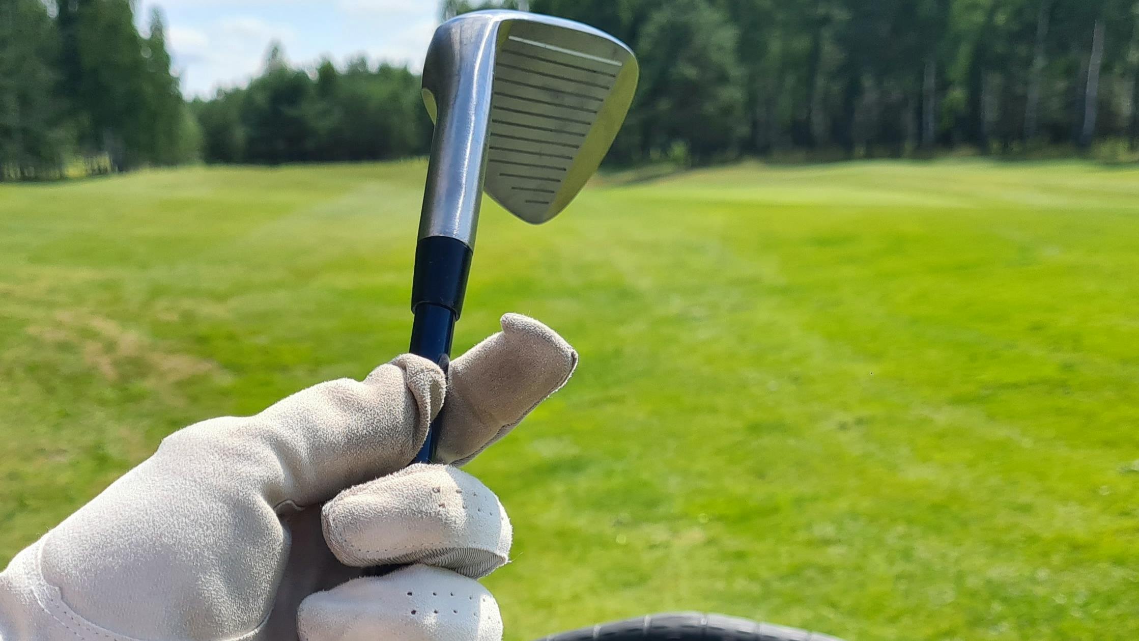 Close up of a golfer holding a golf club by the shaft in a gloved hand. 