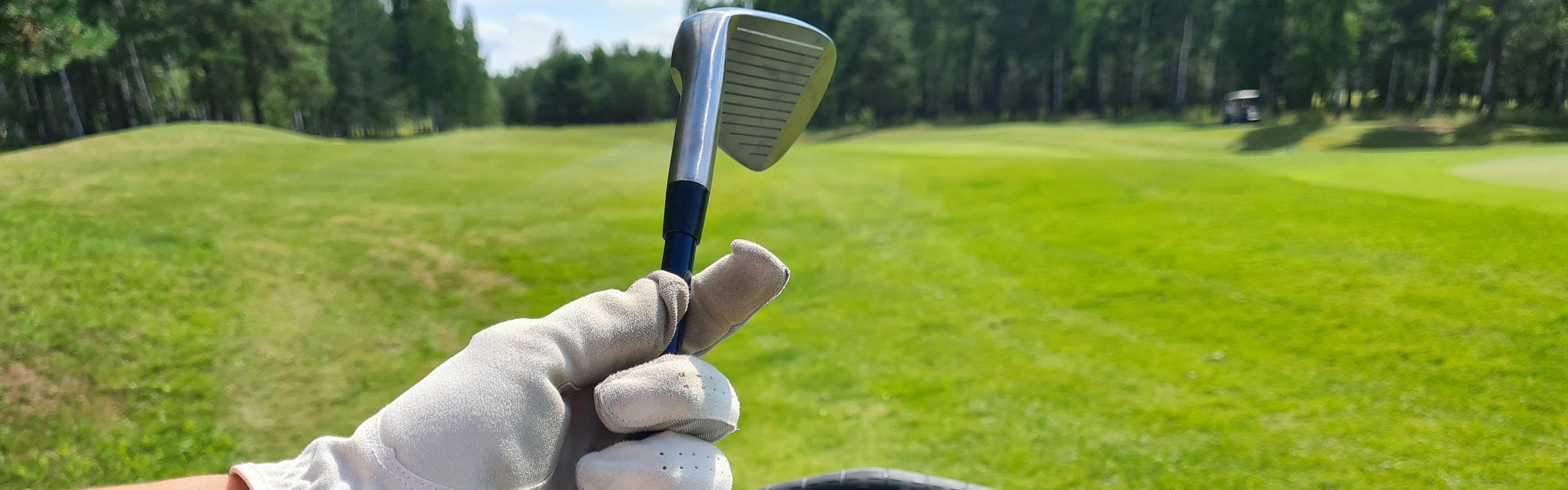 Close up of a golfer holding a golf club by the shaft in a gloved hand. 