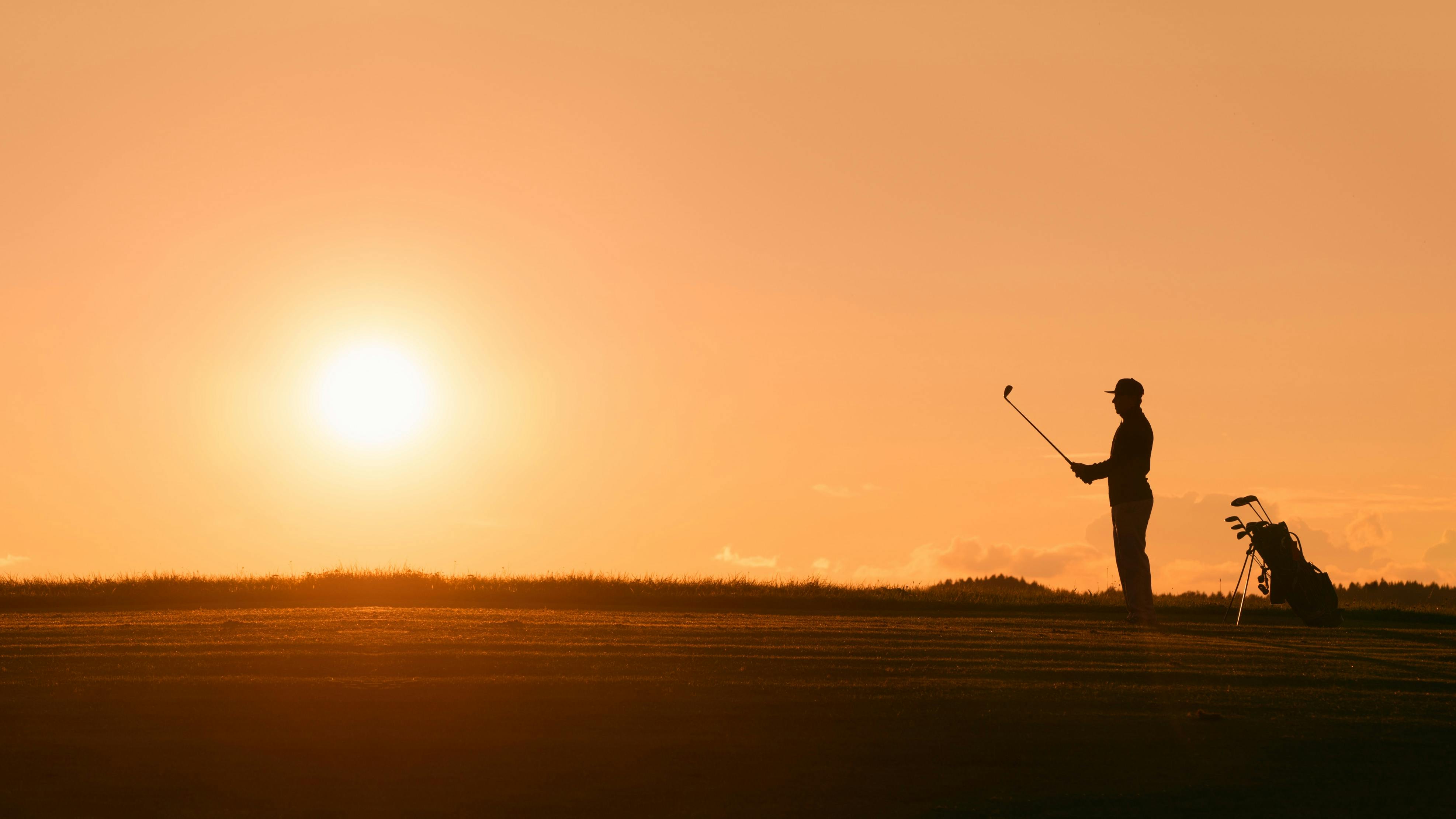 A golfer lining up a golf shot at sundown.