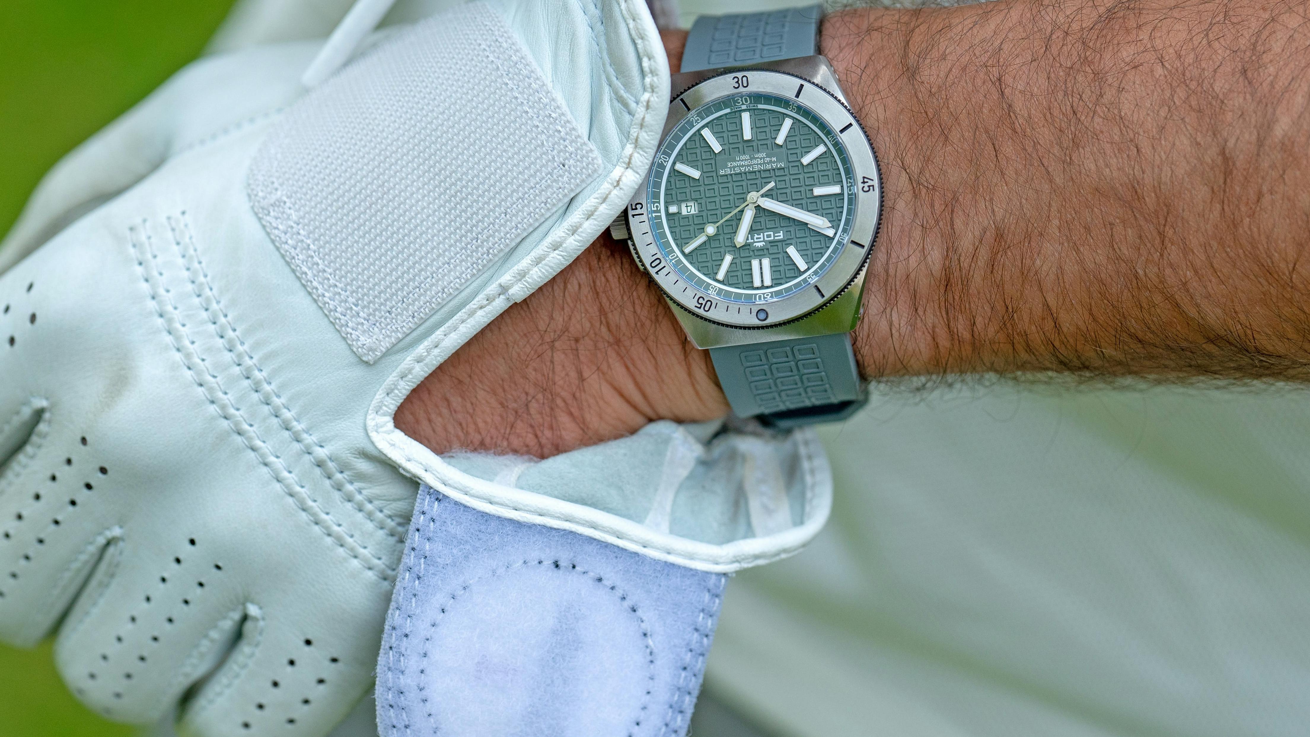 A man slides a golf glove onto his wrist, which already sports a grey watch.