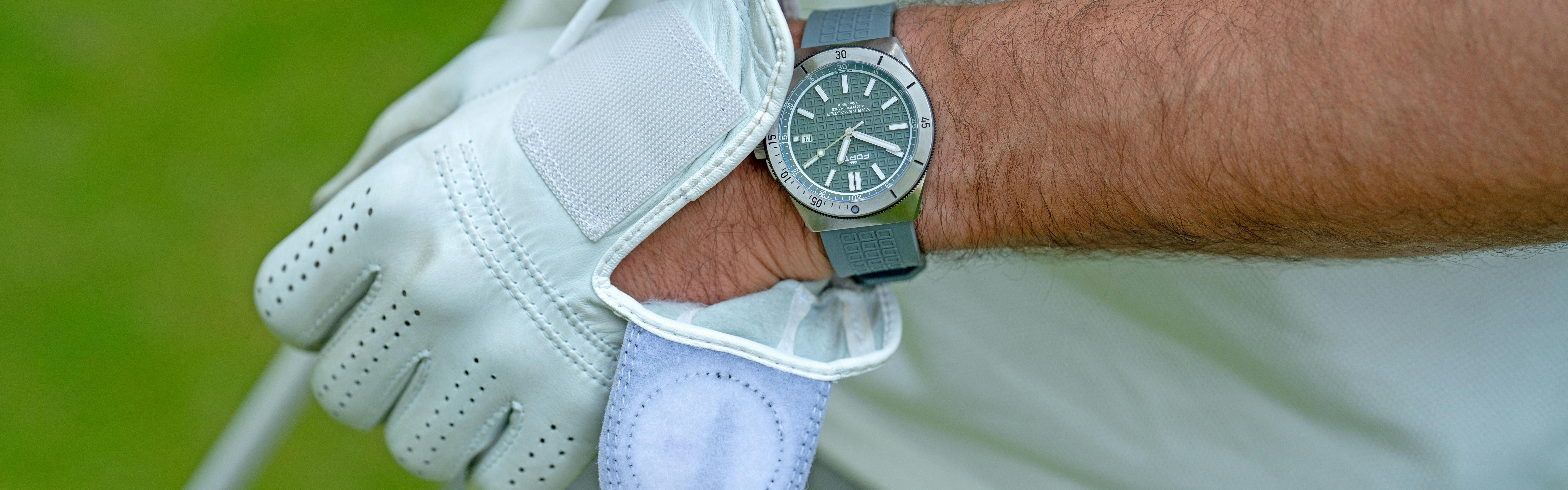 A man slides a golf glove onto his wrist, which already sports a grey watch.