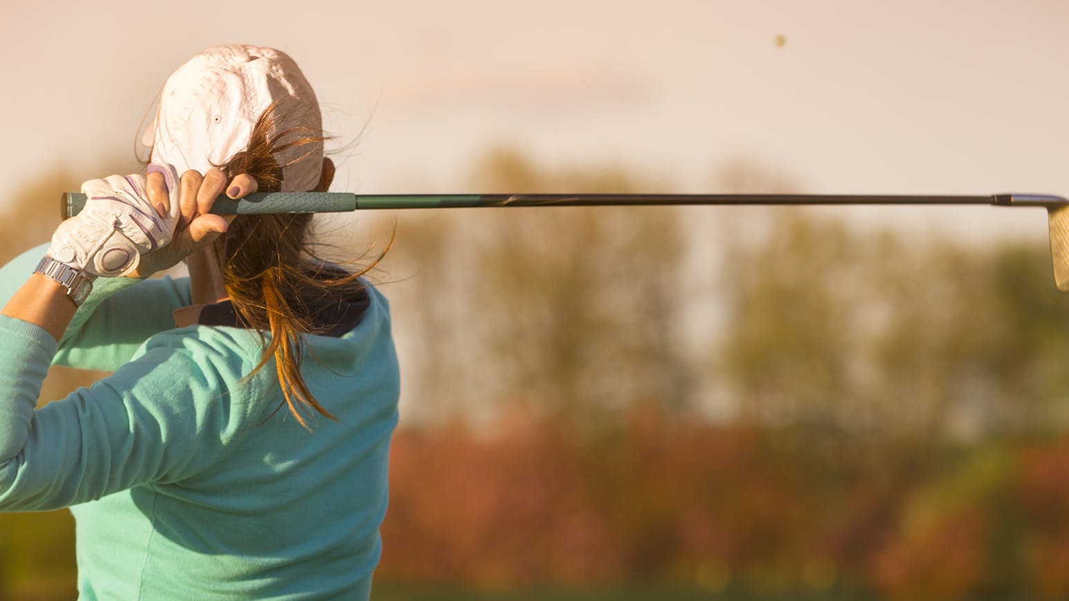 Back view of a female golfer swinging a golf club. 