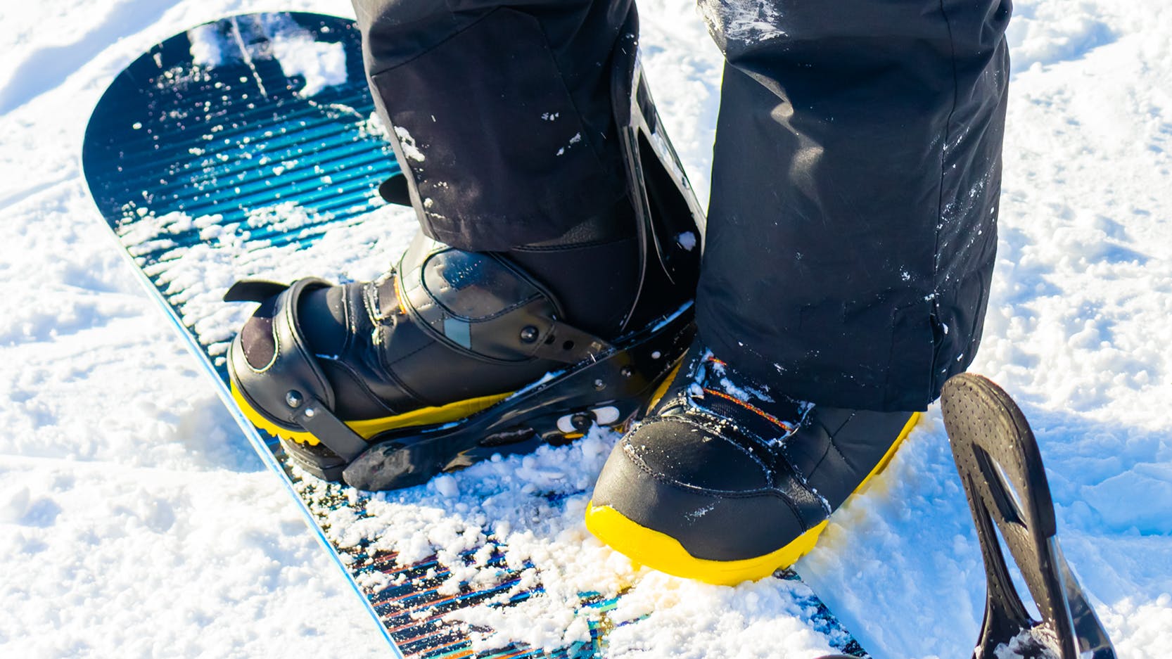 Close up of a snowboarders boots as he stands on his snowboard. 