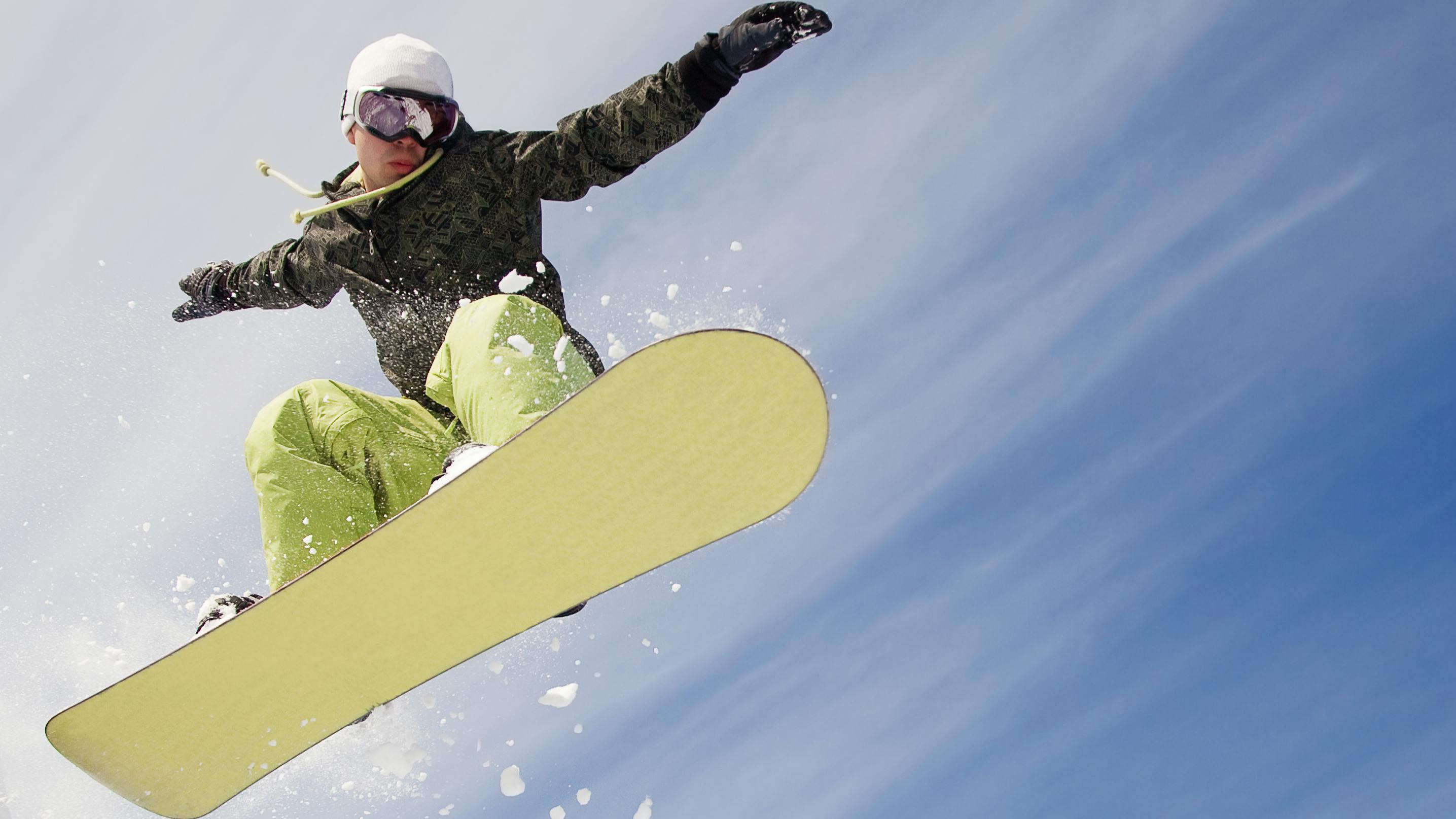 A snowboarder goes off a jump. His hands are outstretched and the bottom of his snowboard is visible. 