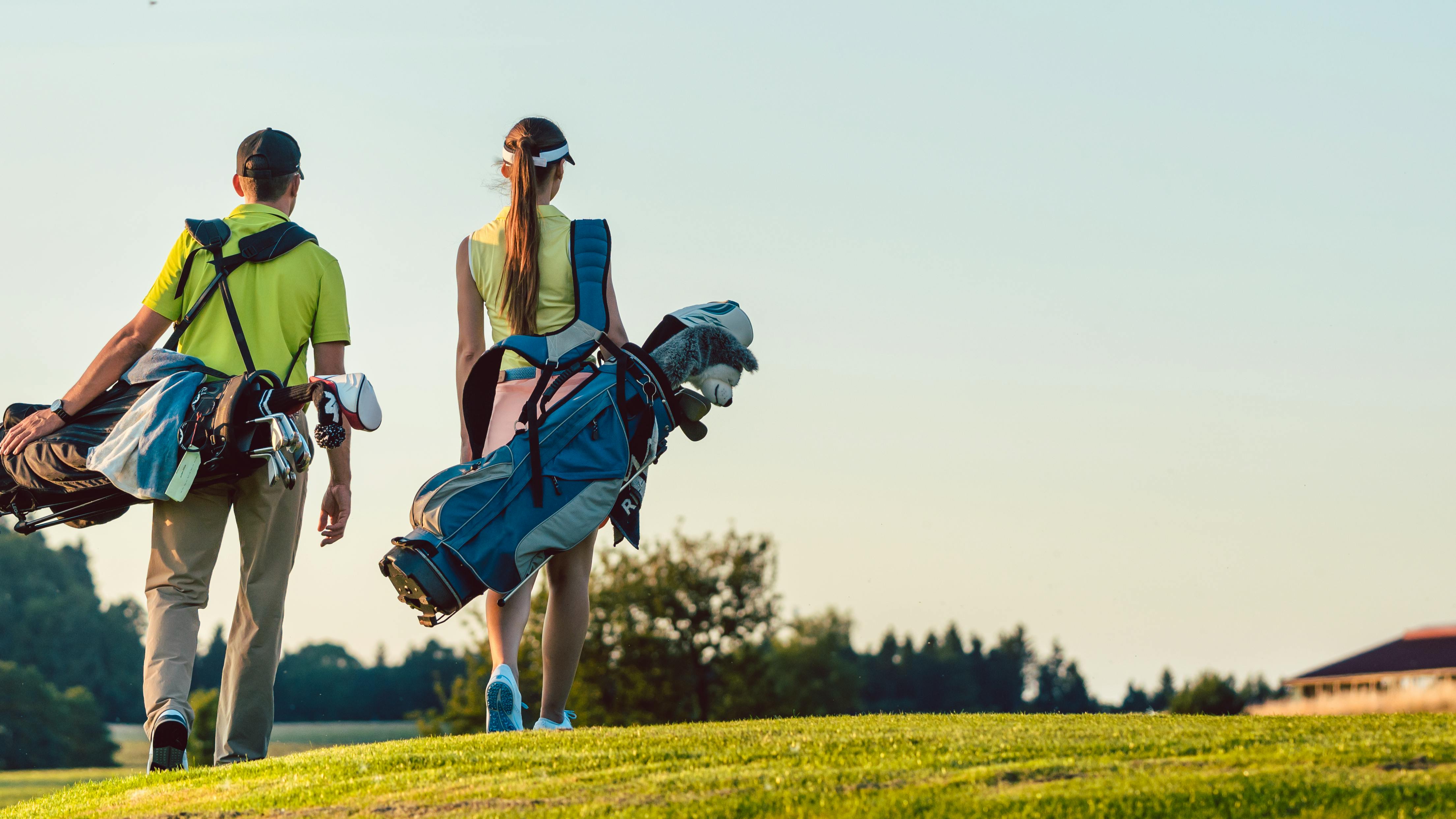 Two golfers walking on a golf course while carrying their golf bags. 
