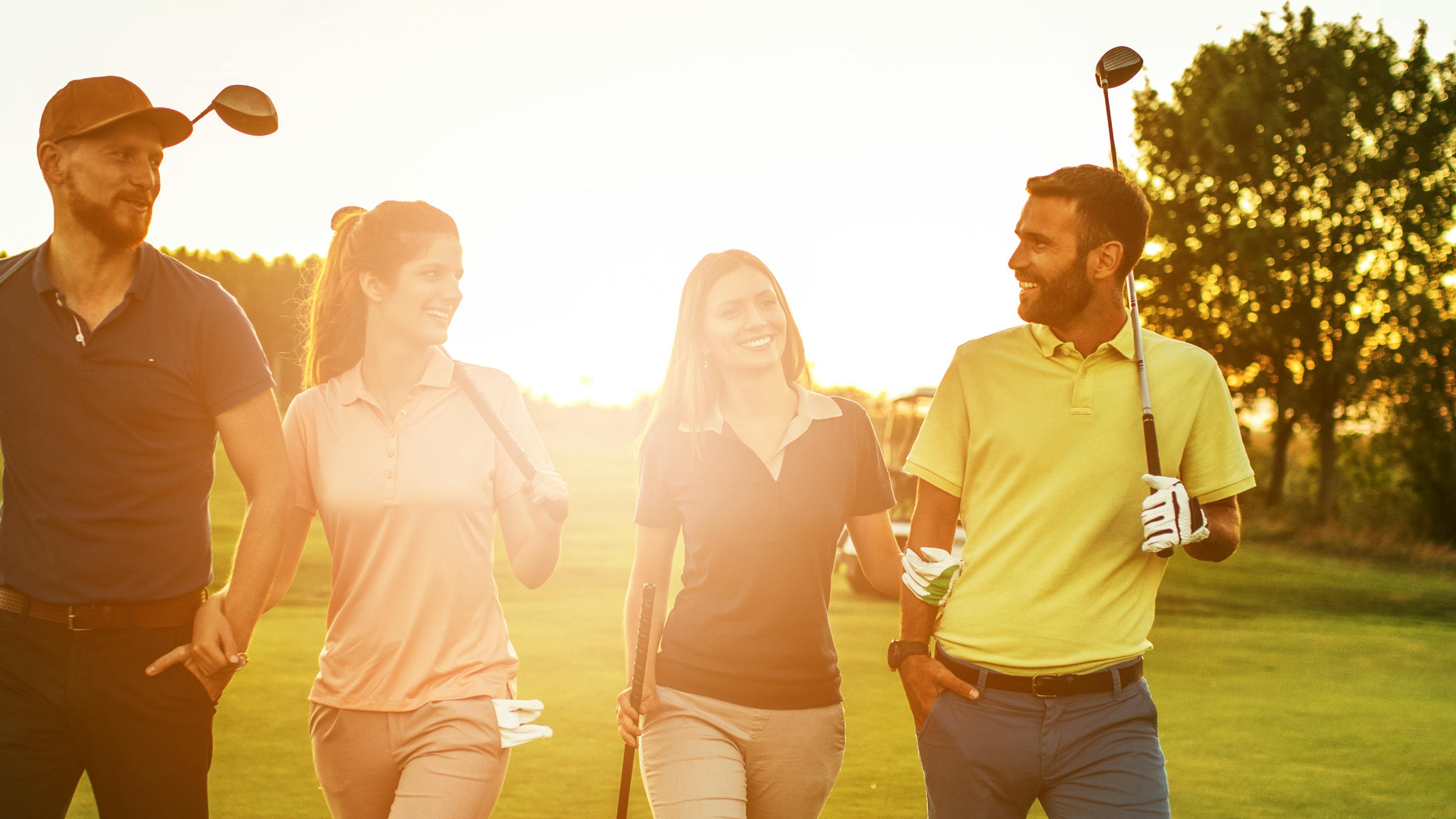 Four golfers walking along a golf course while holding their clubs. 