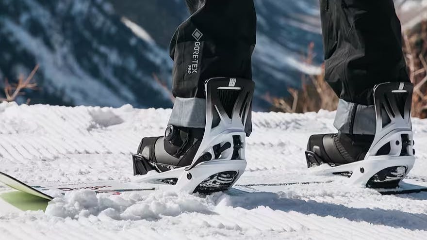 A snowboarder standing at the top of a snowy run with his boots in his bindings. 