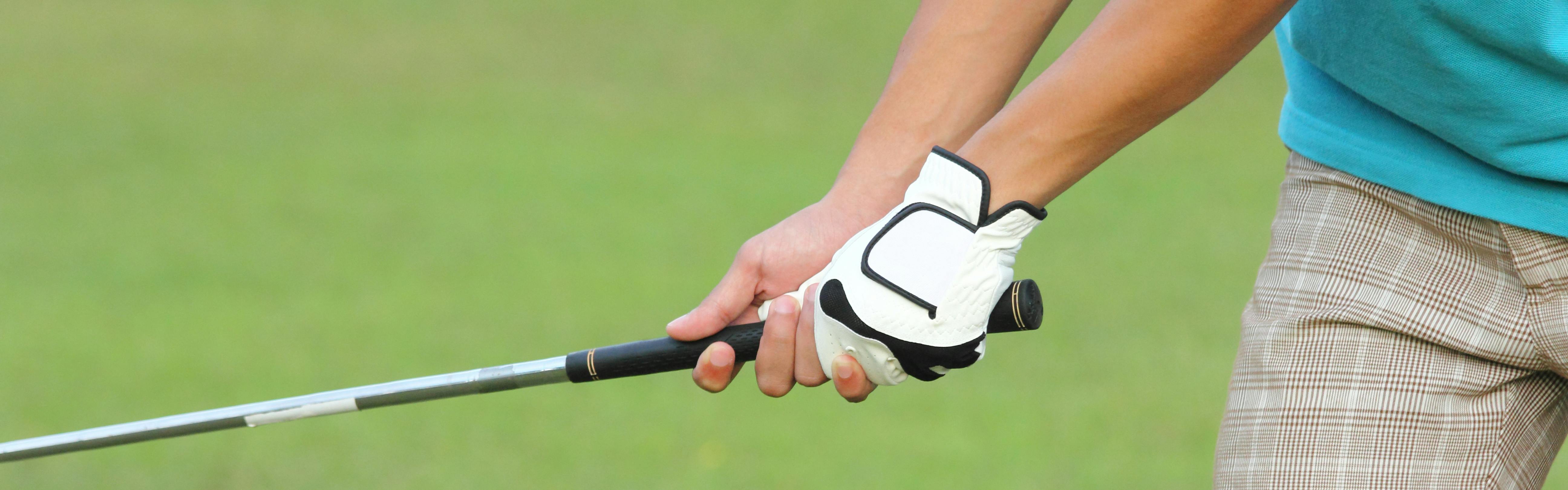 A golfer holding a golf club with one gloved hand. 