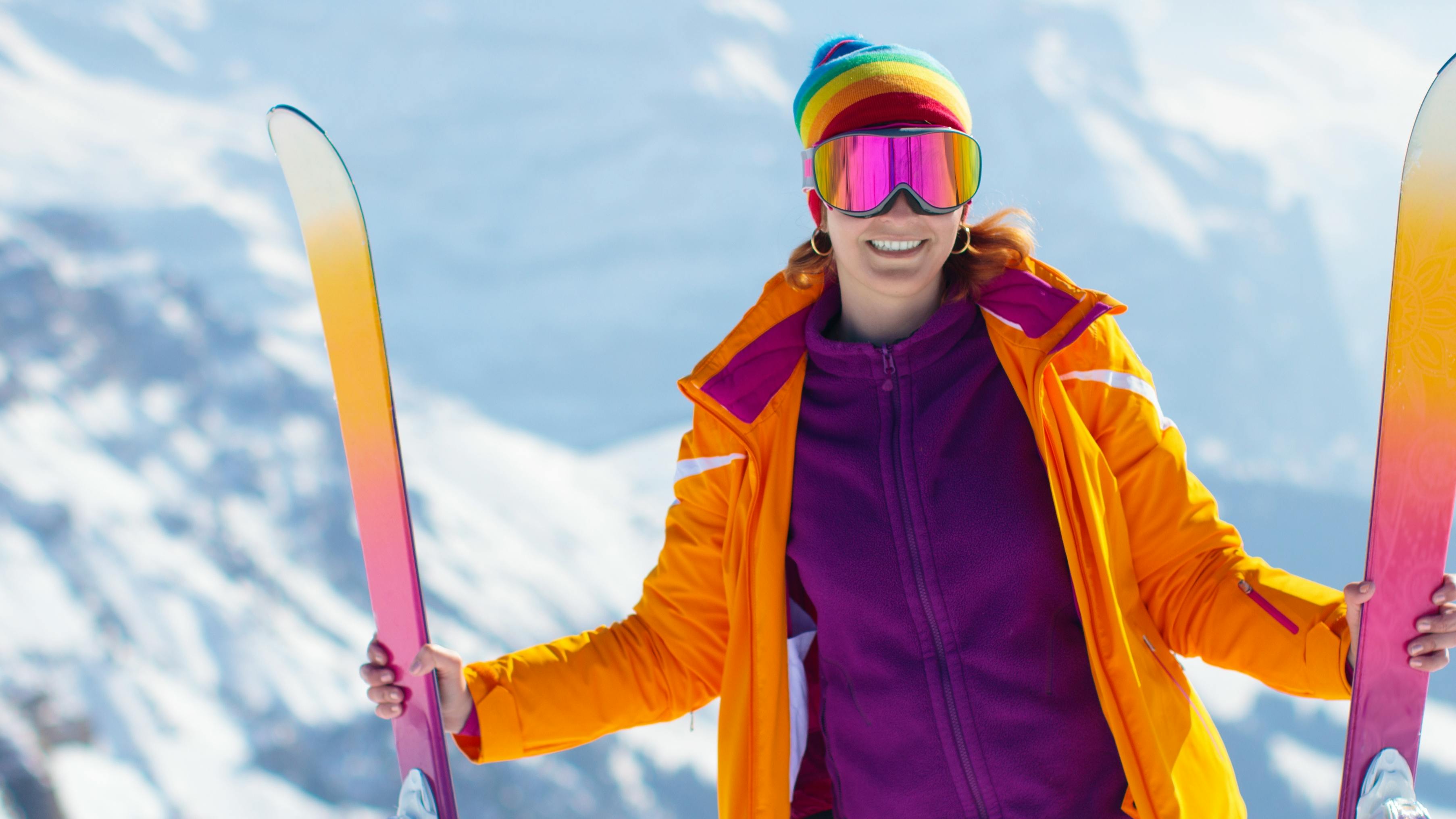 A female skier standing at the top of a ski mountain holding her skis next to her. 