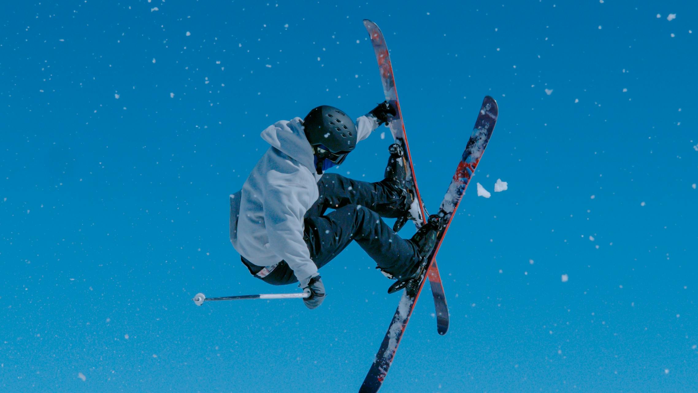 A skier jumping in the air as he grabs his ski.