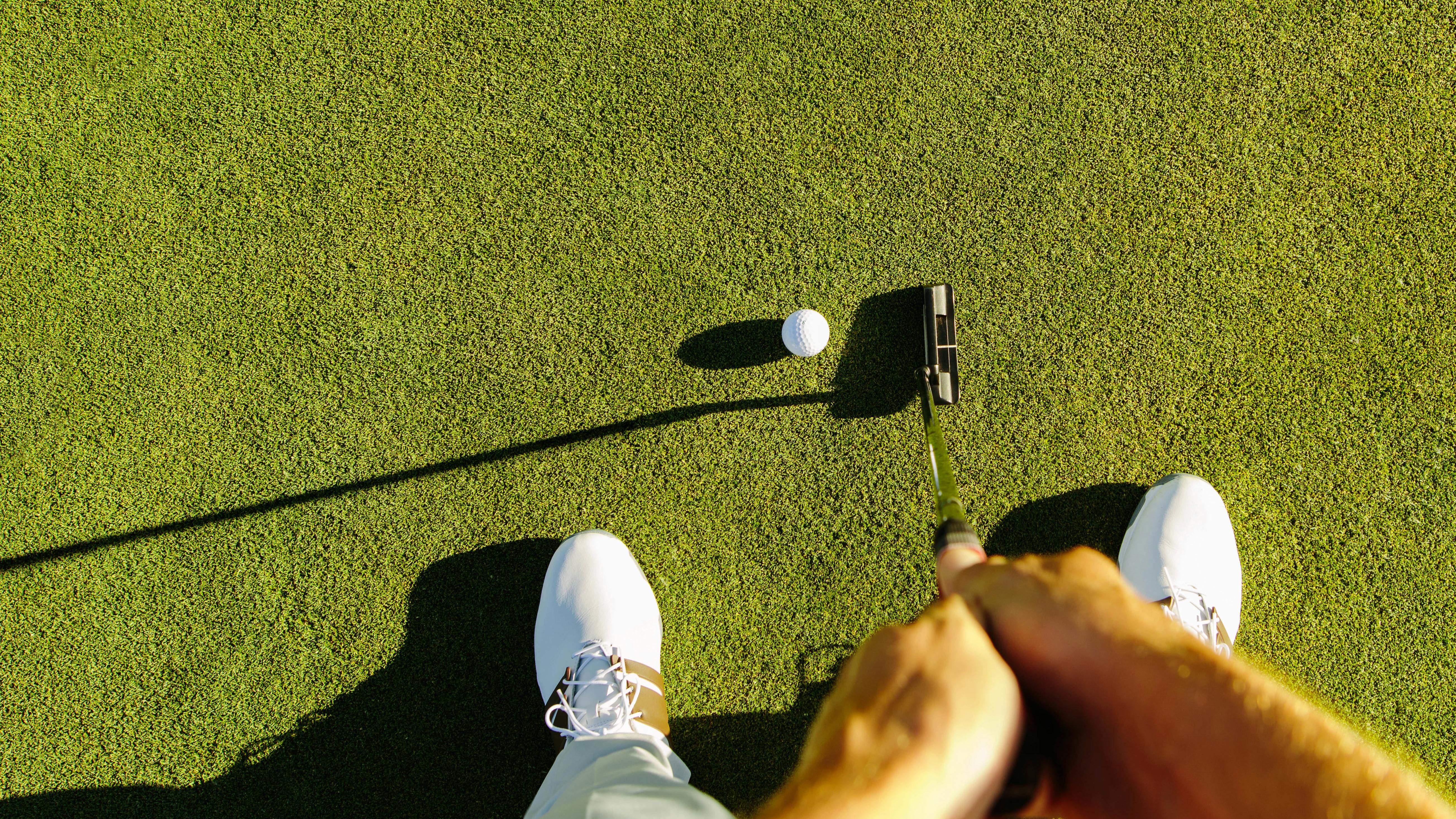 Top down view of a golfer putting a ball into the hole. 