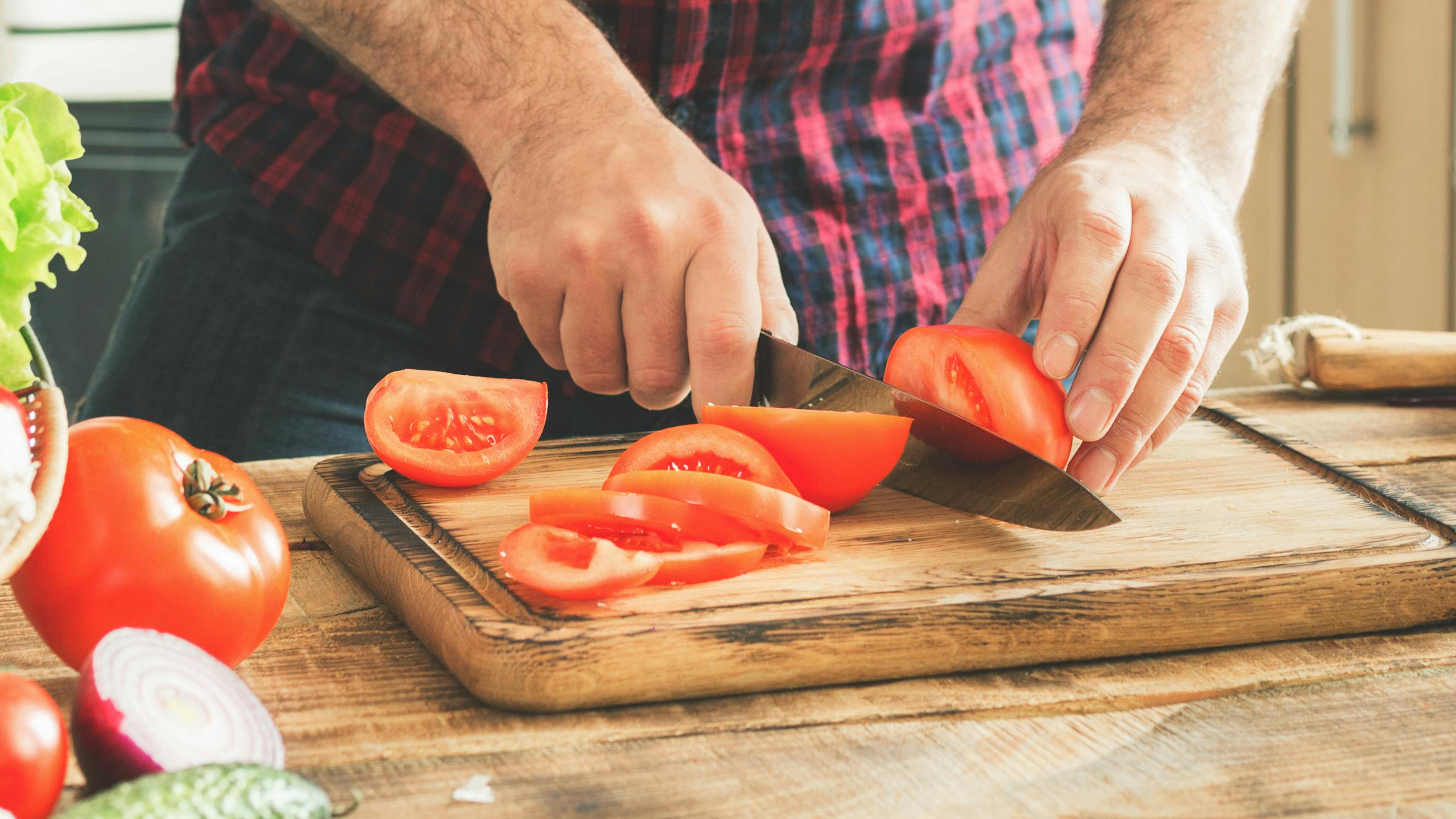 A man cutting a tomato on a cutting board.