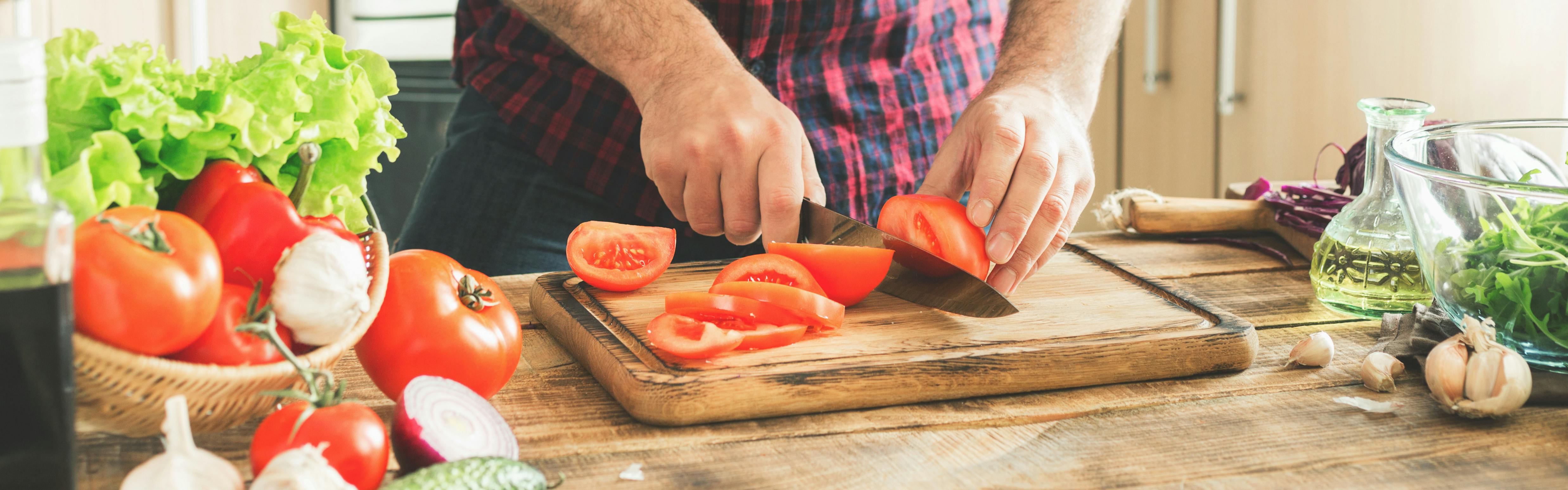 A man cutting a tomato on a cutting board.