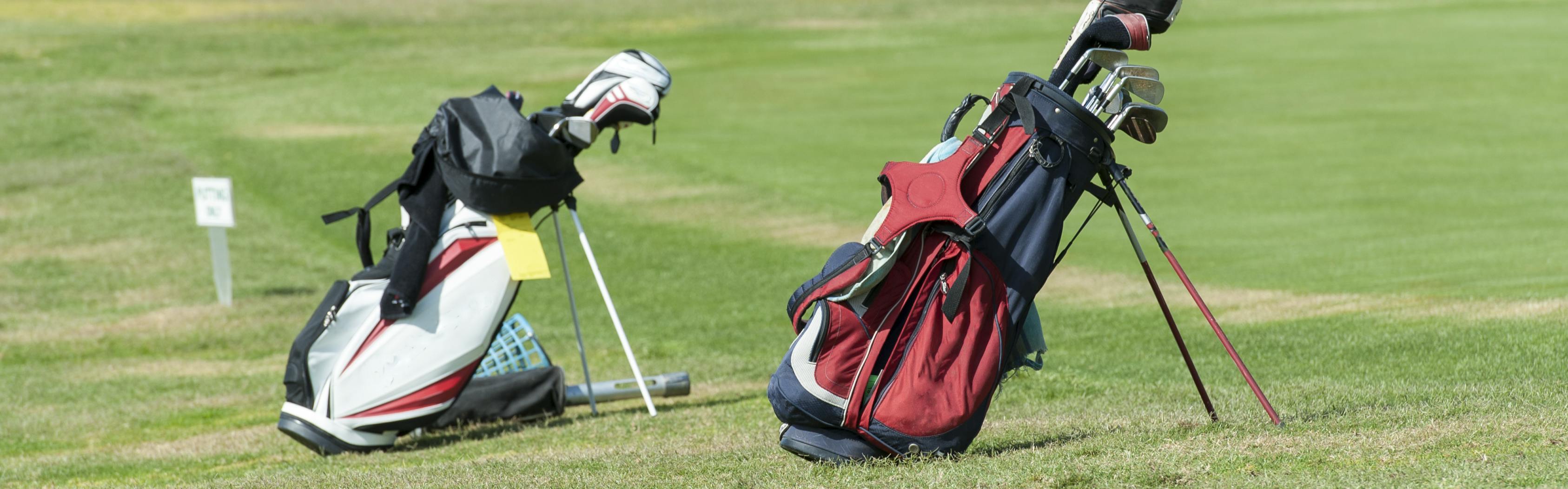 Two golf bags sitting on grass. One is red white and blue and one is red and white.