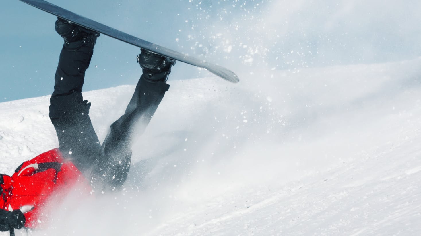 A snowboarder falling with his back on the snowy ground and his snowboard in the air. 