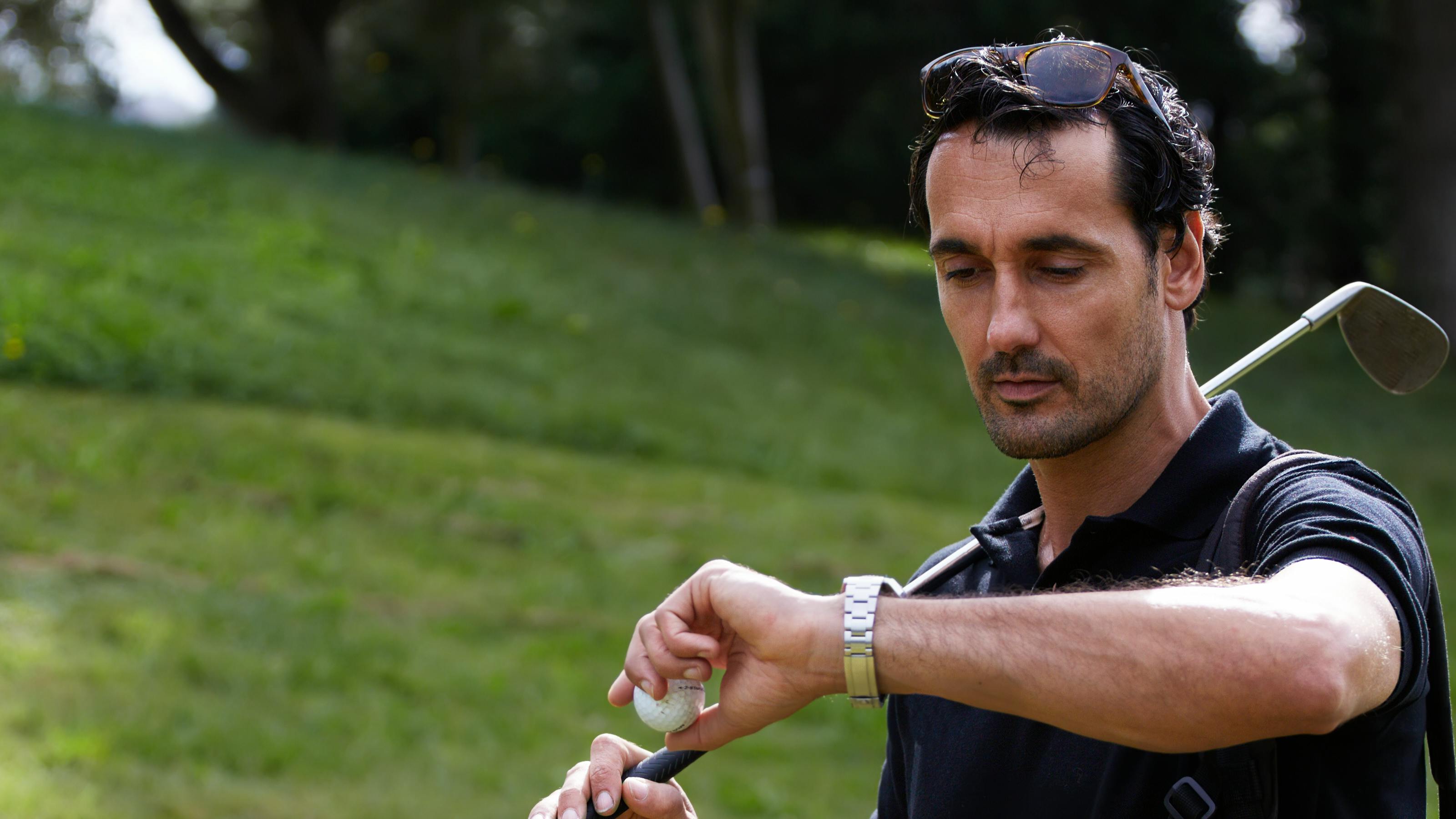 A golfer holding a club checks his watch. 