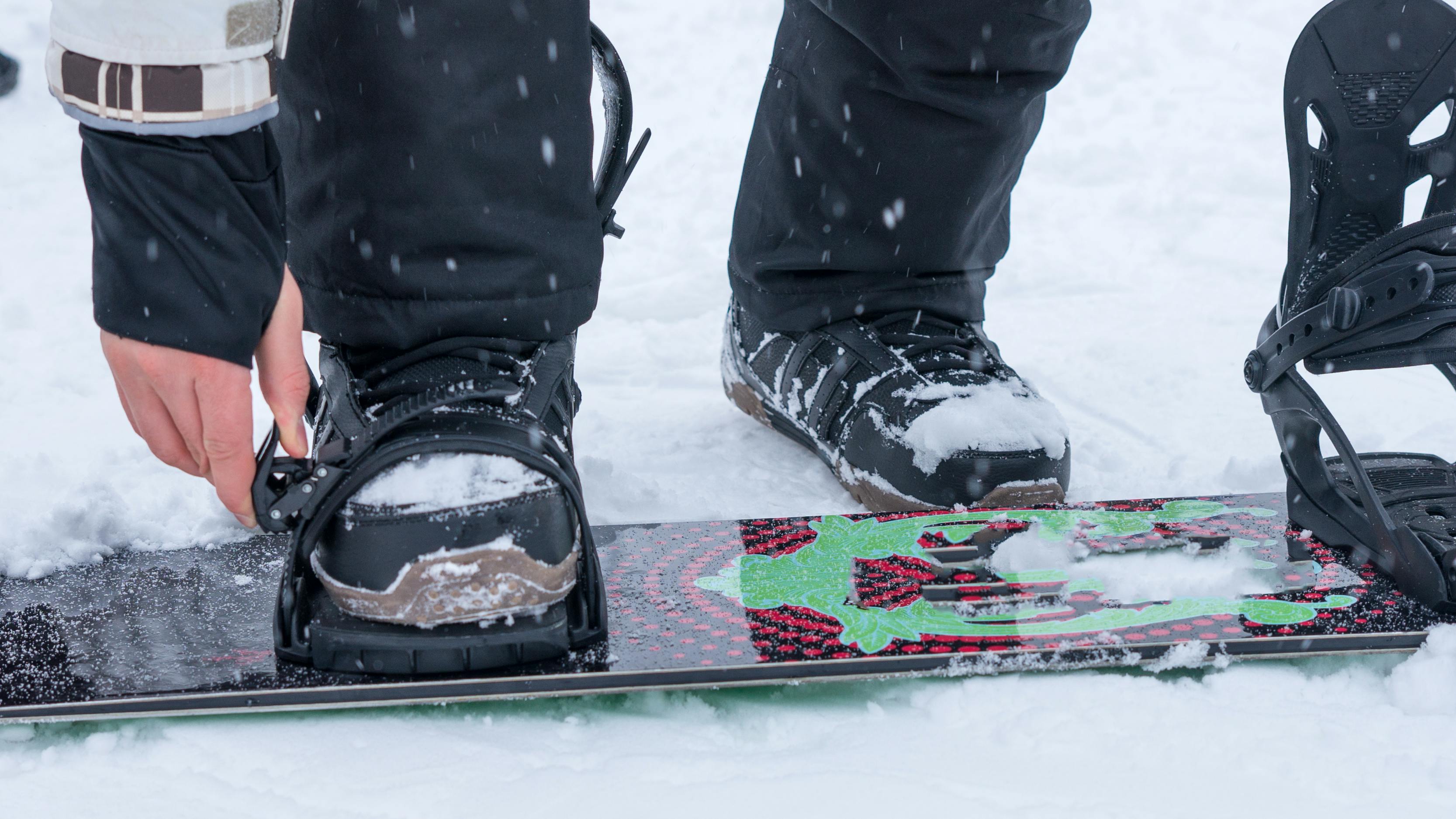 A snowboarder attaching his boots into his snowboard bindings.