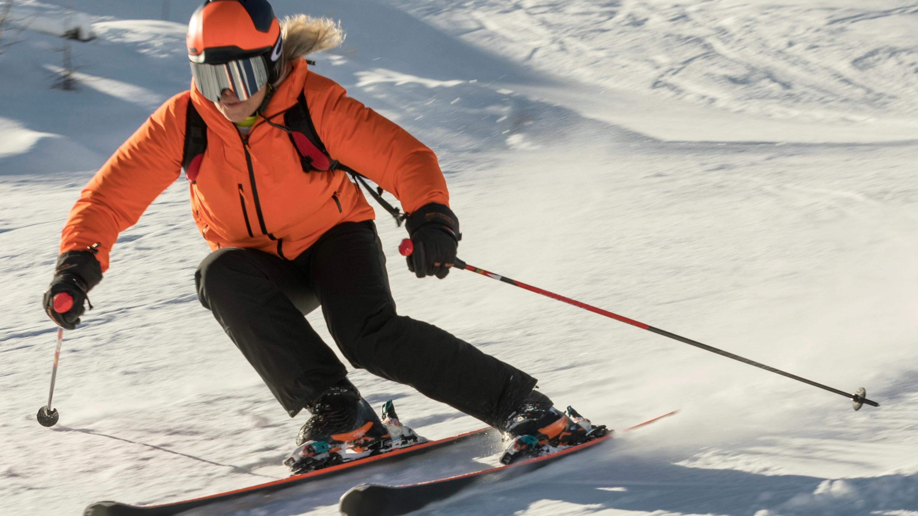 A skier turning down a ski run in an orange jacket and an orange and black helmet. 
