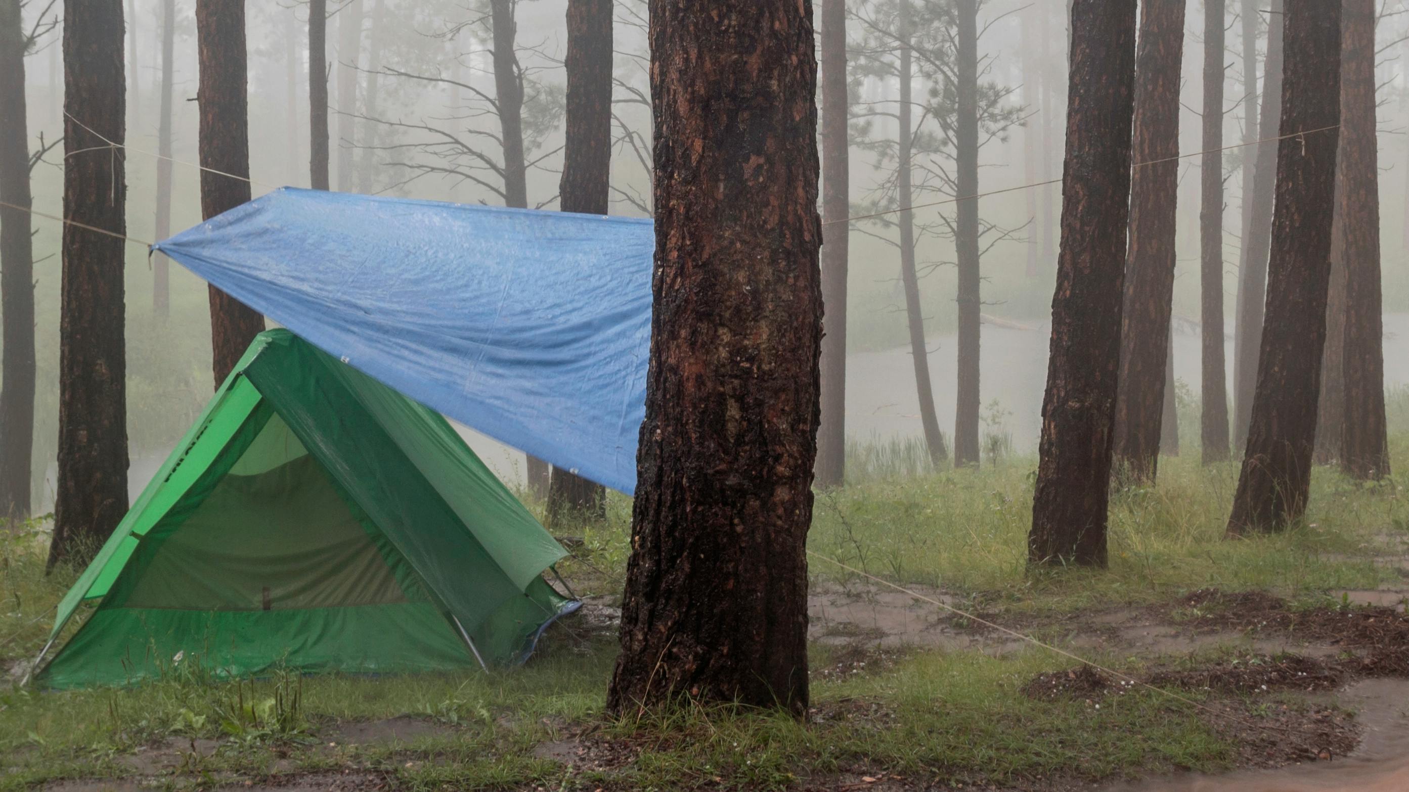 A tent in the rain with a tarp over it.