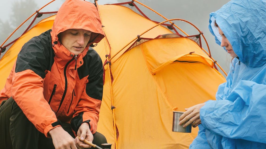 Two campers making food in the rain.