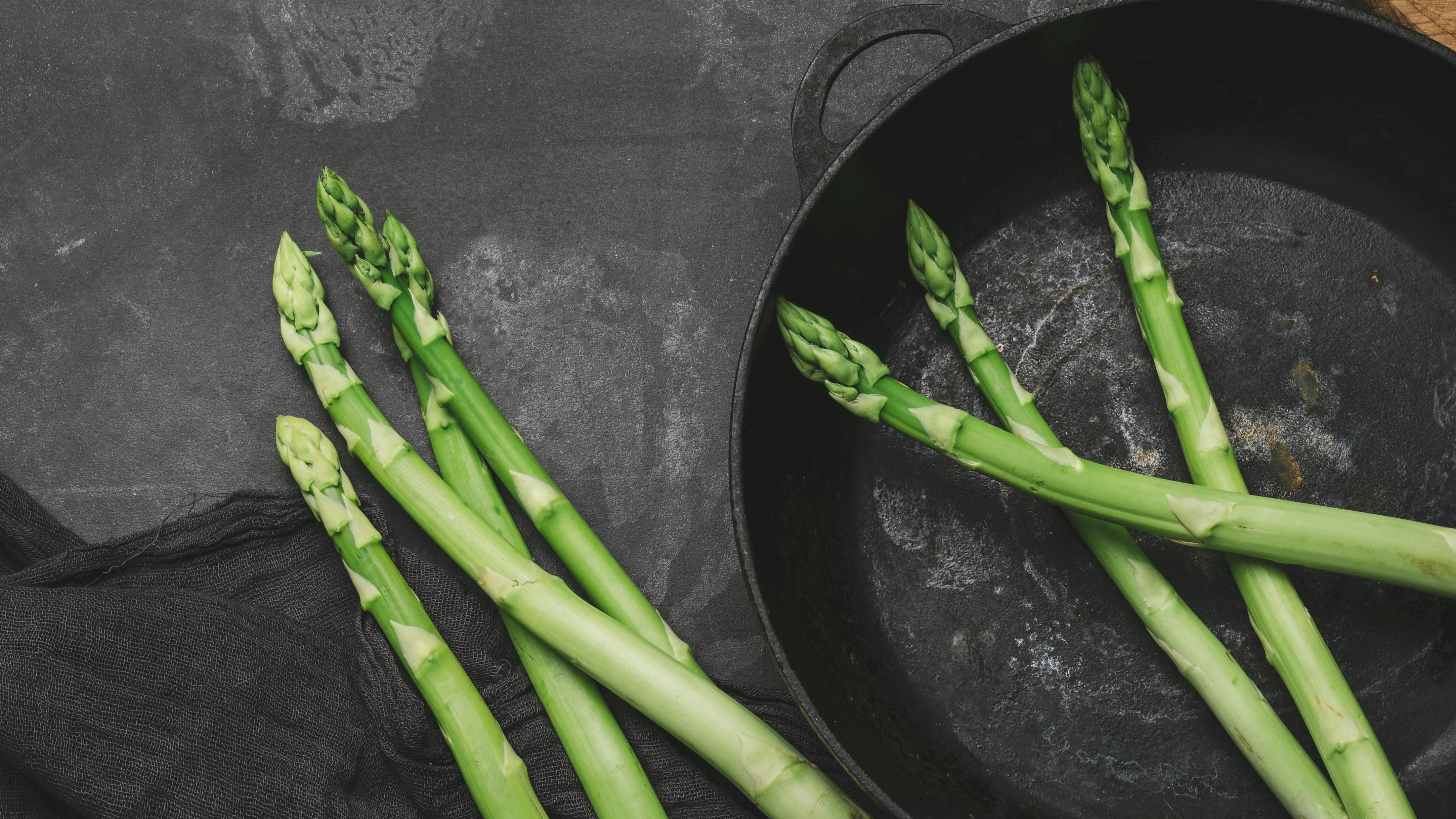 Raw asparagus in a cast iron pan as other stalks of asparagus sit next to it out of the pan. 