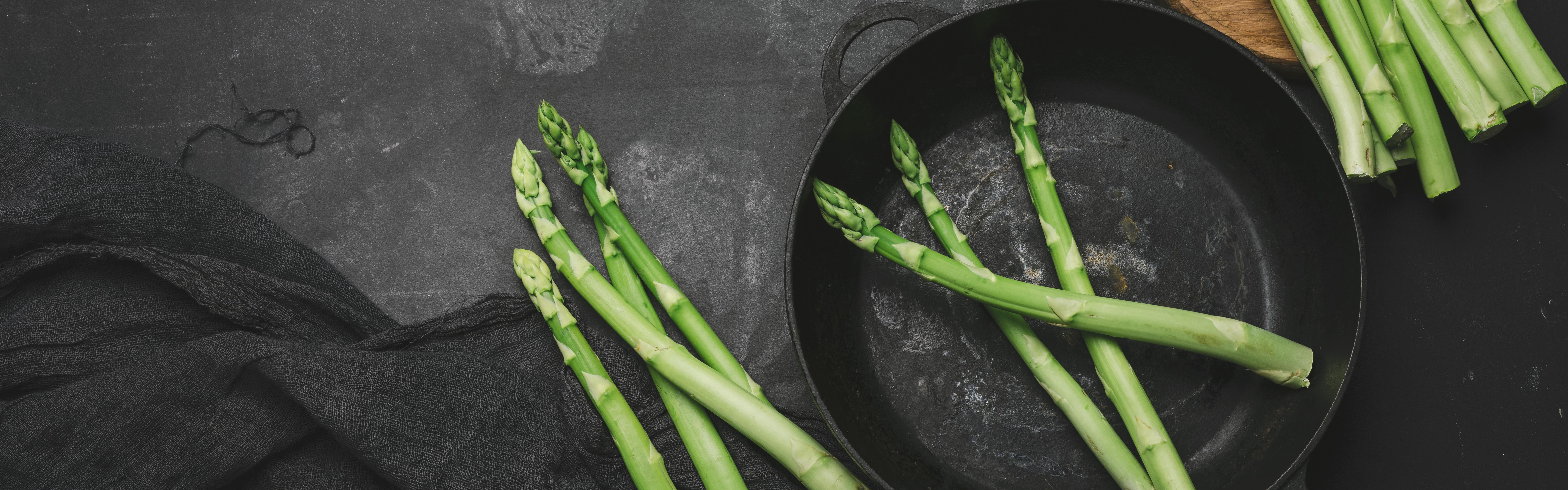 Raw asparagus in a cast iron pan as other stalks of asparagus sit next to it out of the pan. 
