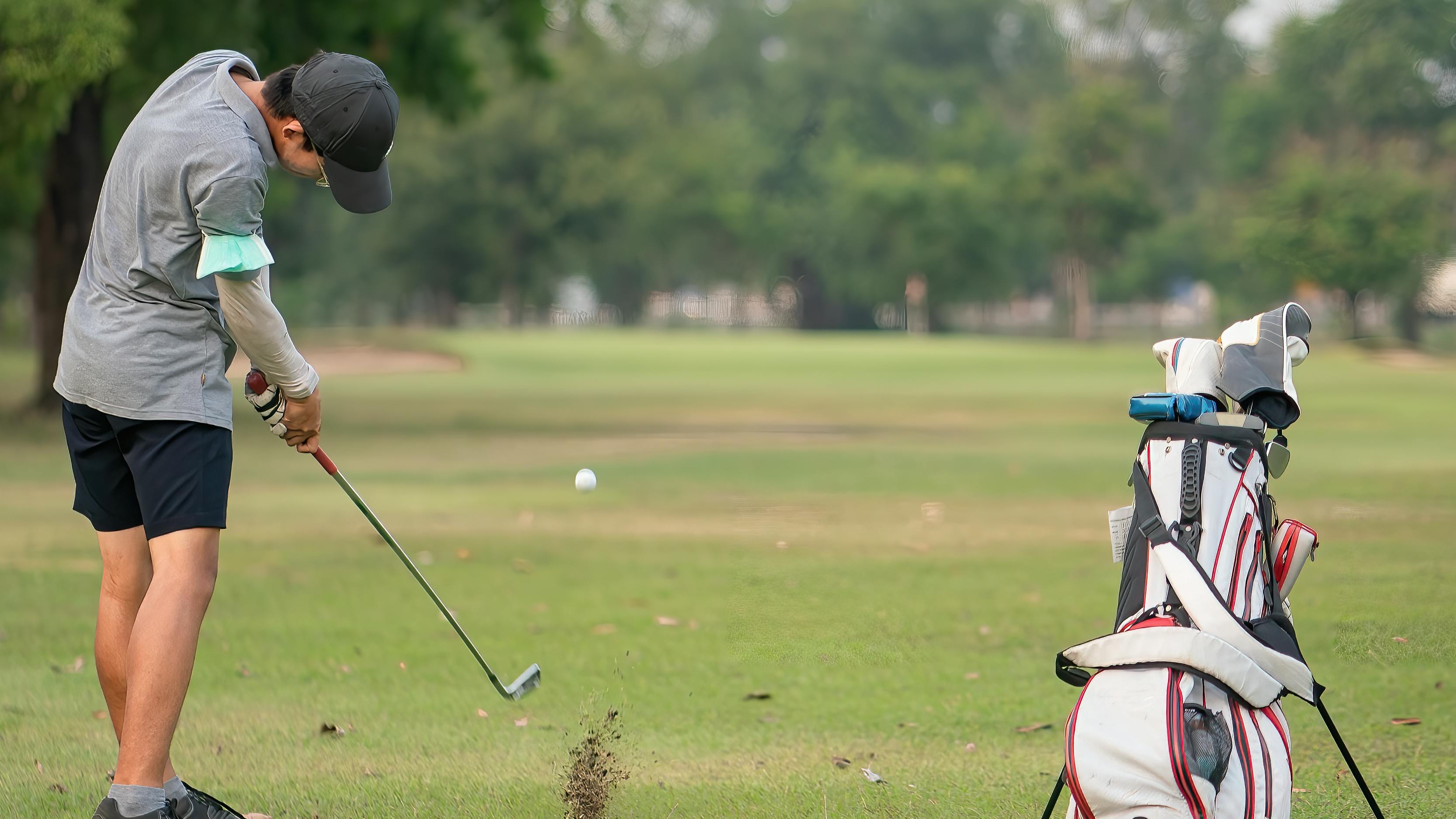 A golfer using an iron on a golf course. 