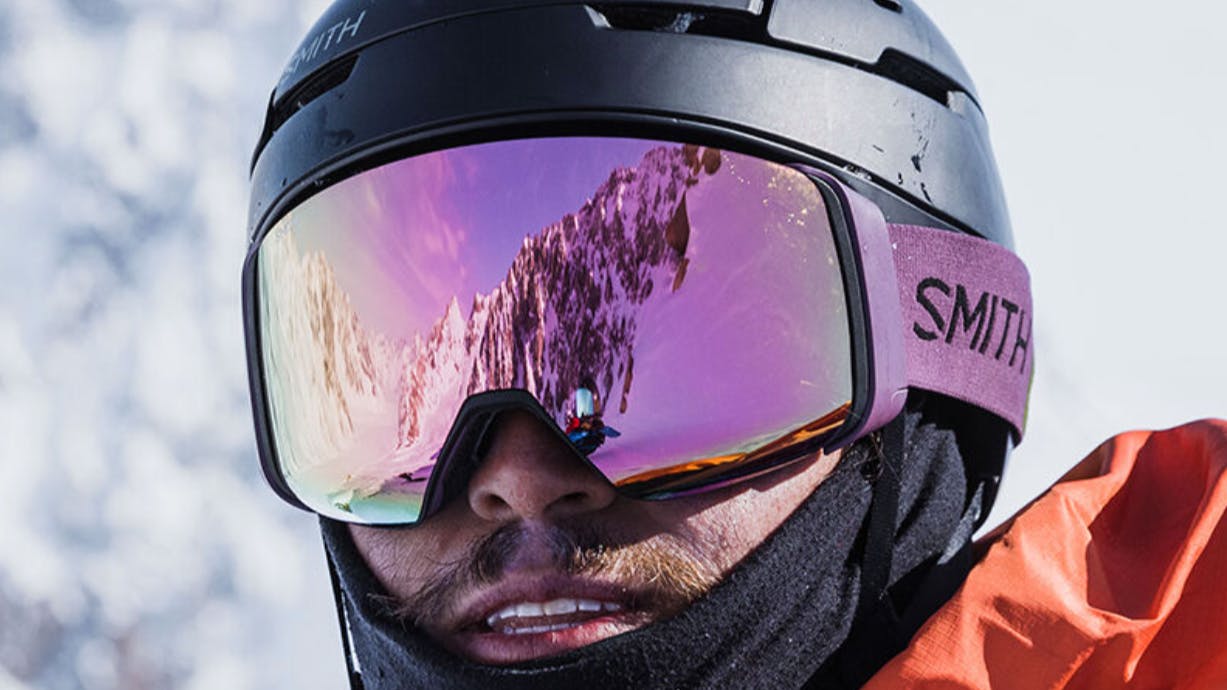 A snowboarder wearing Smith Goggles as he looks at the camera. 