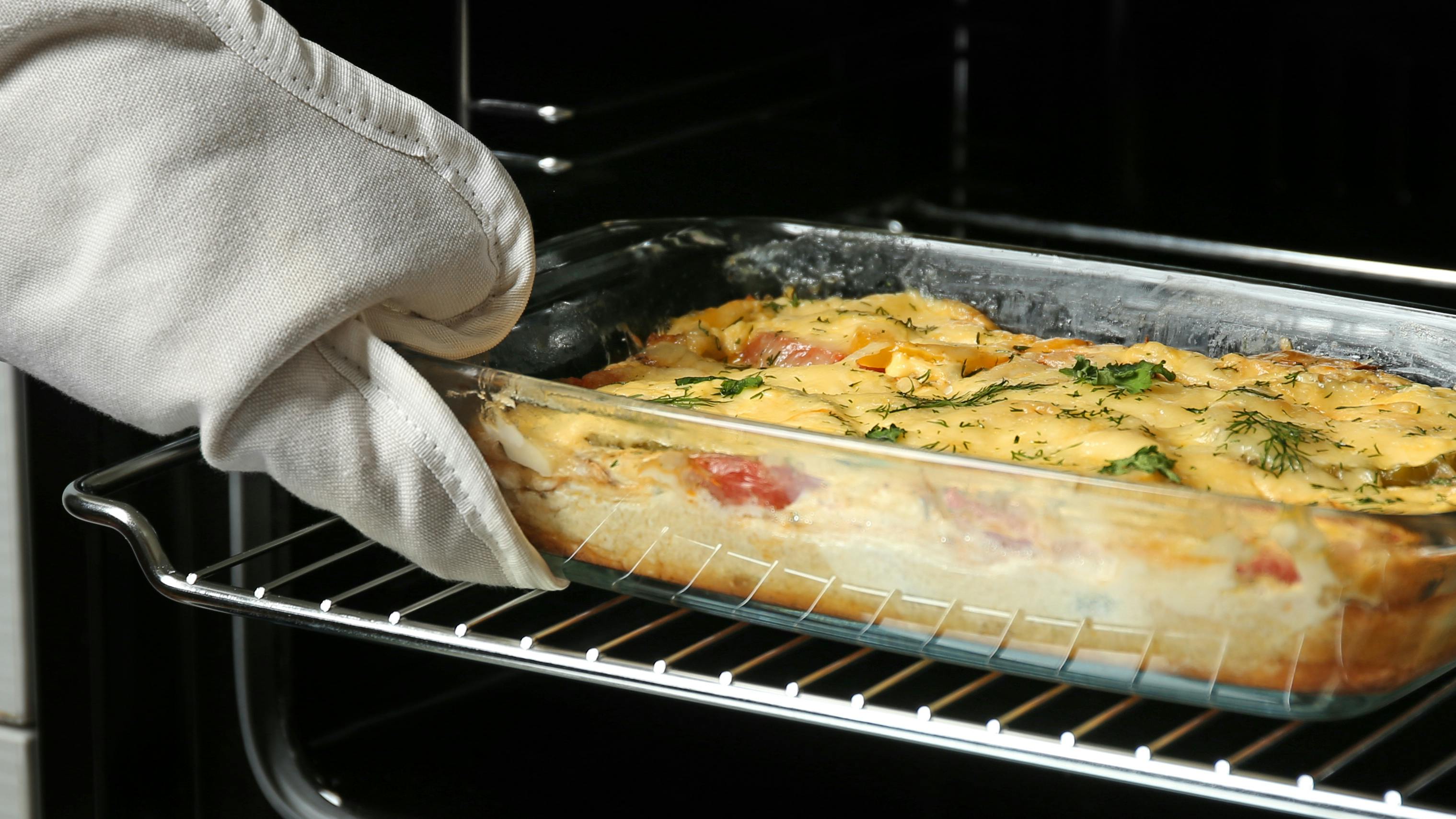 A woman putting a baking dish in an oven. 