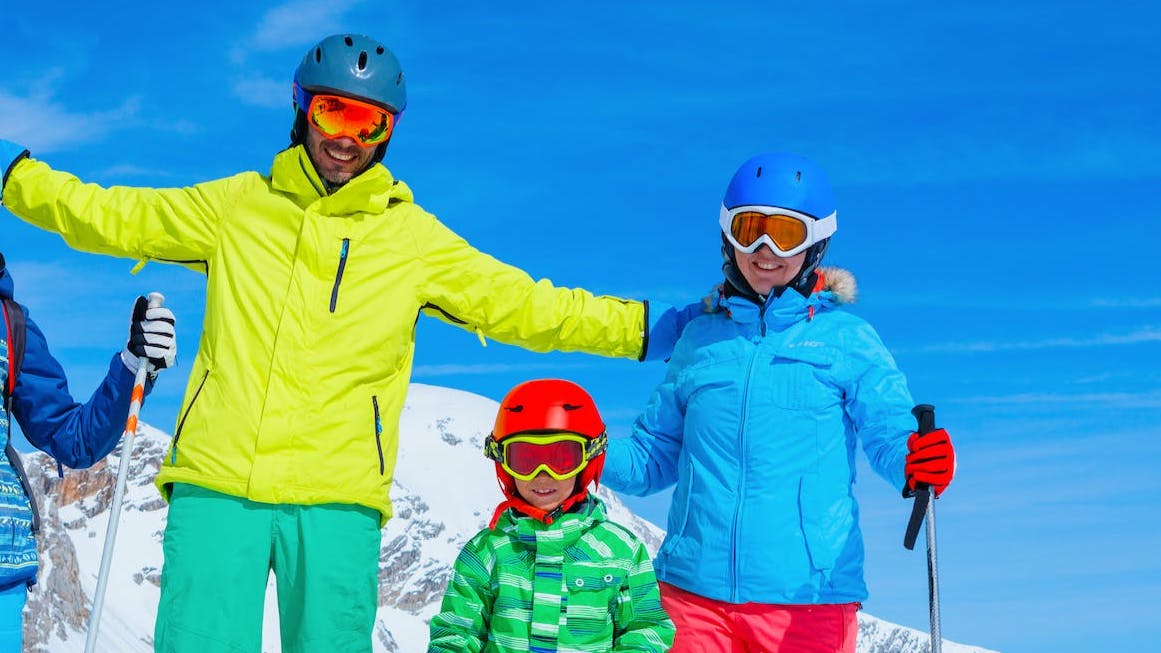 A family in ski gear stands at the top of a snowy mountain. 